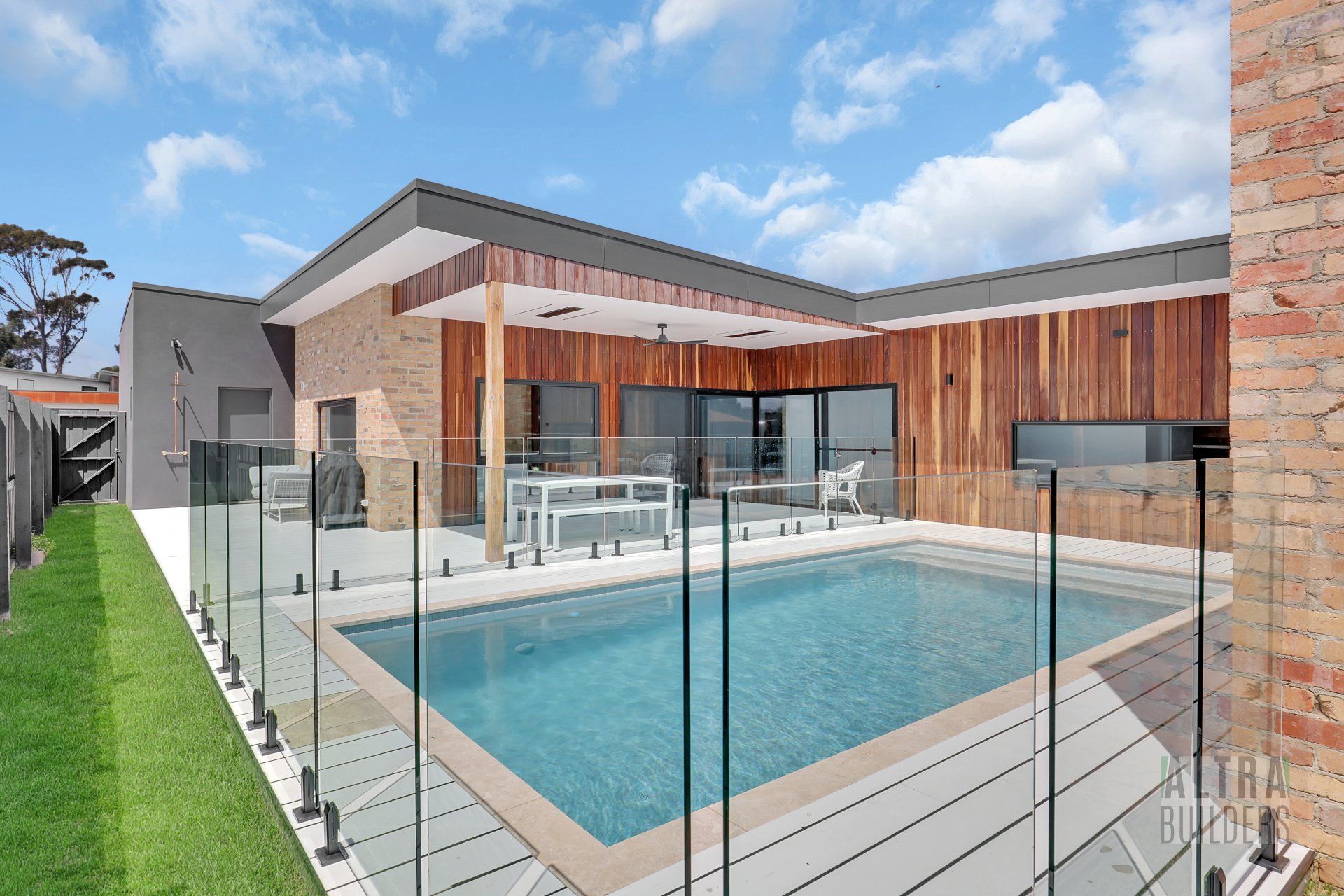 A large swimming pool is surrounded by a glass fence in front of a house.