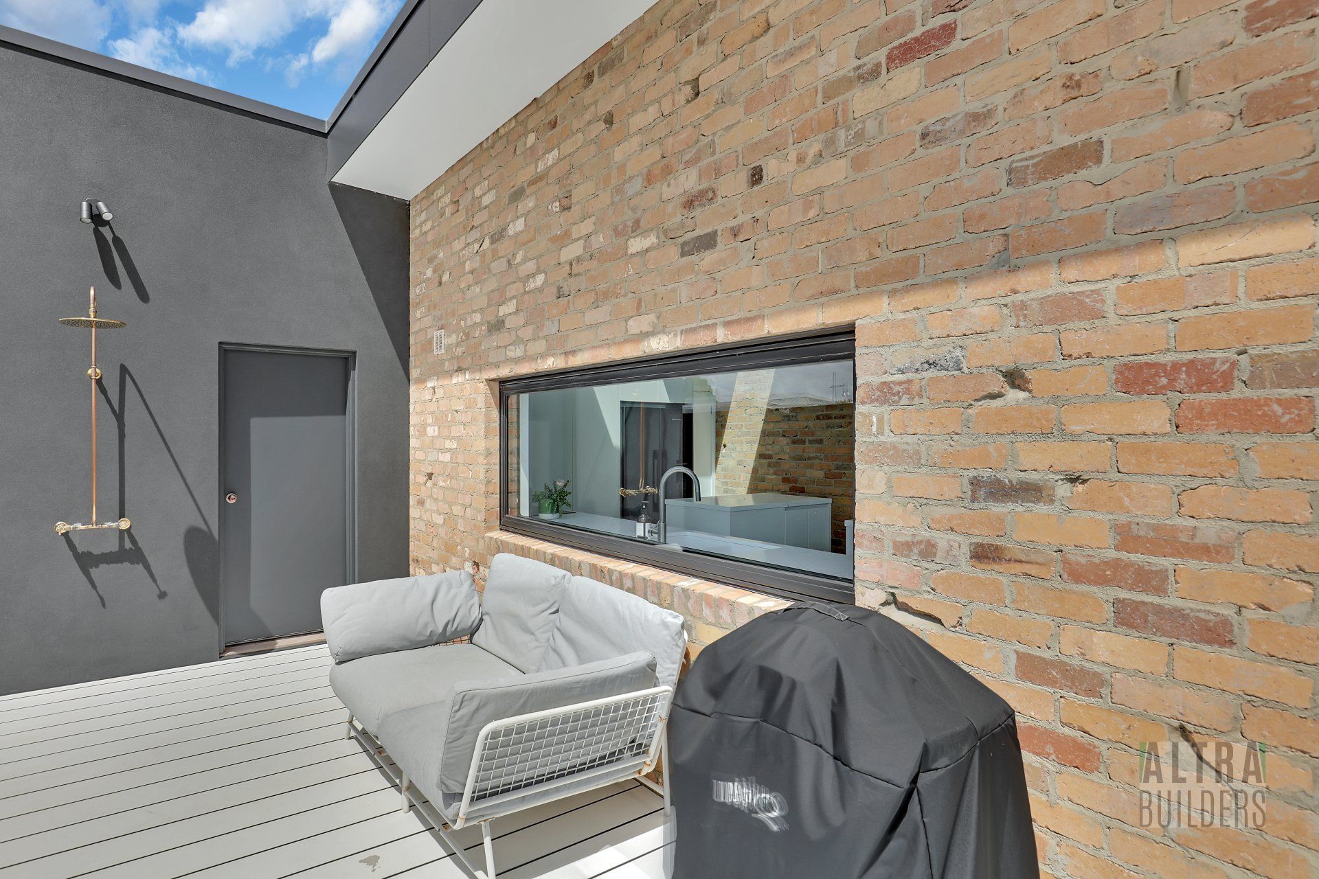 A patio with a couch and a grill in front of a brick wall.