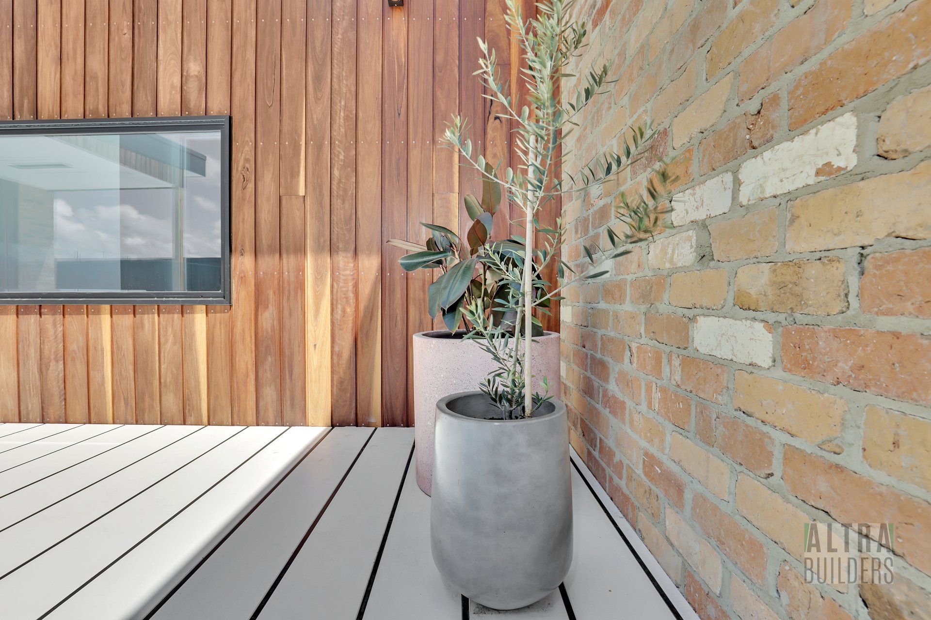 A potted plant is sitting on a wooden deck next to a brick wall.