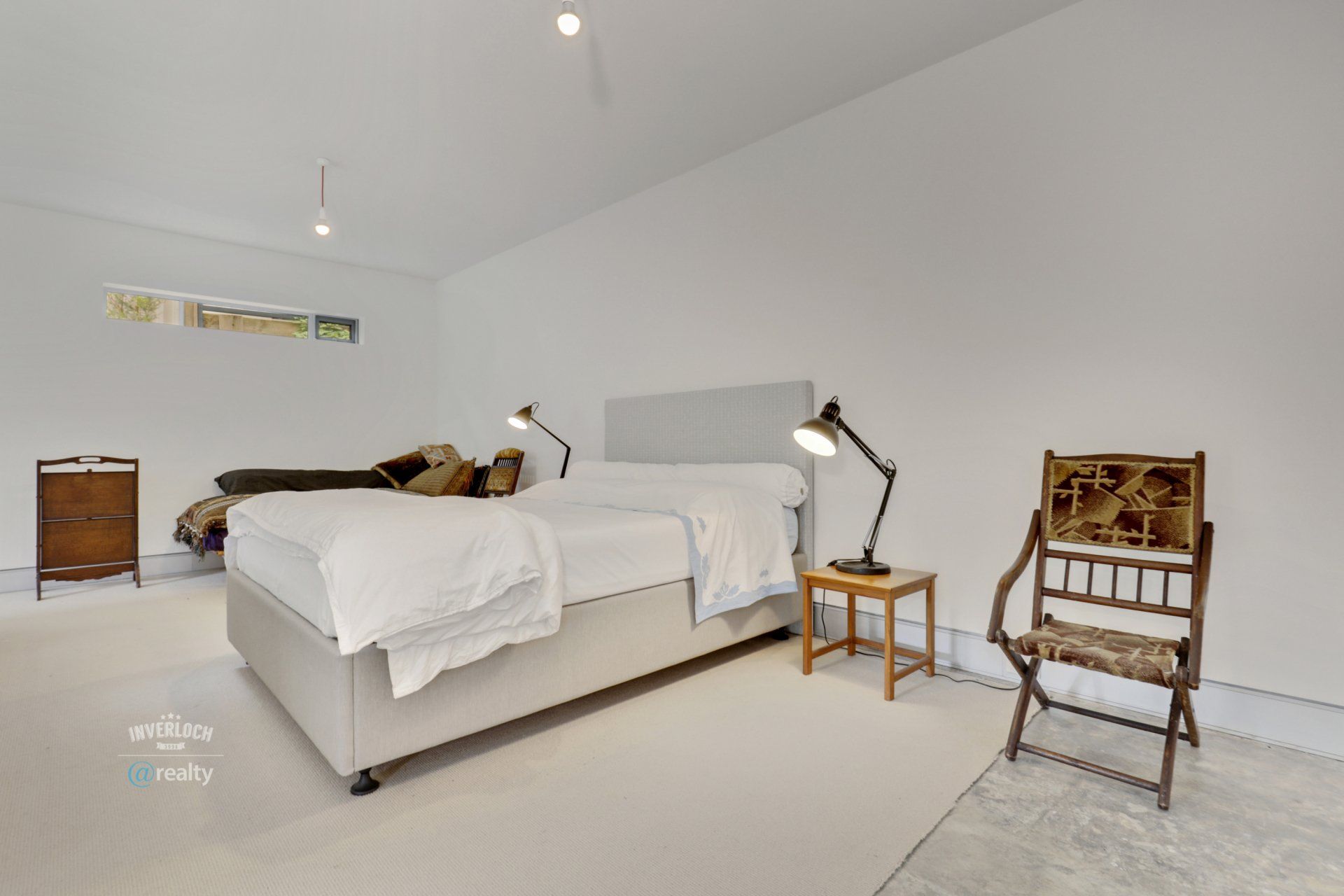 A bedroom with a bed , chair , nightstand and lamp.