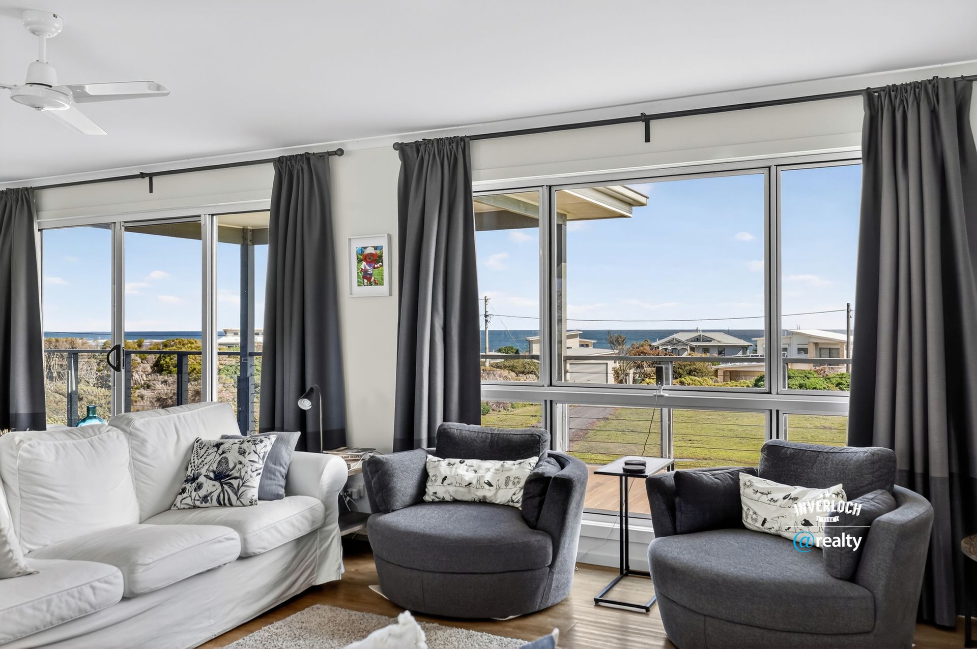 Living room with ocean view, white sofa, gray armchairs, and curtains.