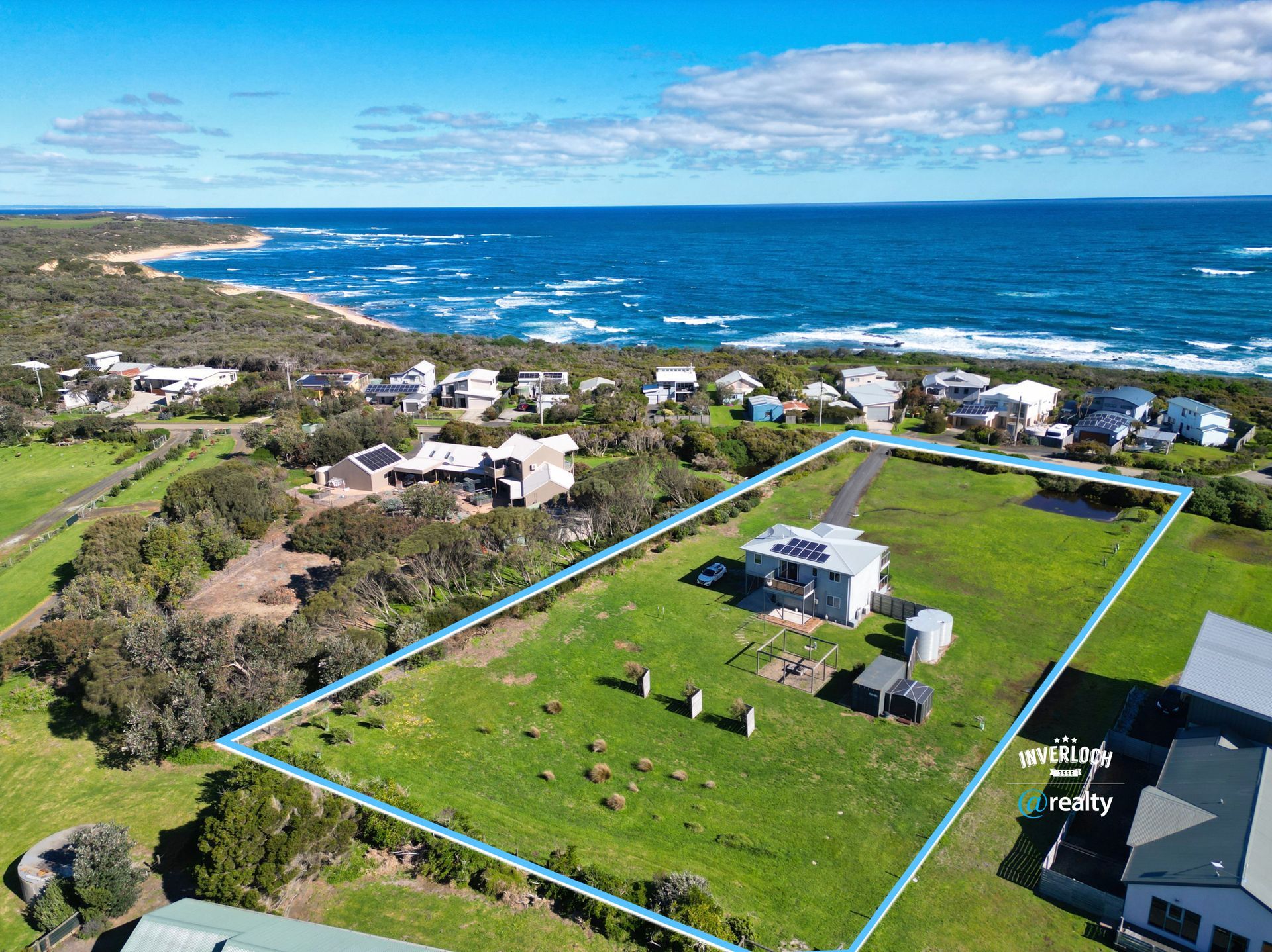 Aerial view of a house on a large grassy lot near the ocean. Blue outlined property with solar panels.