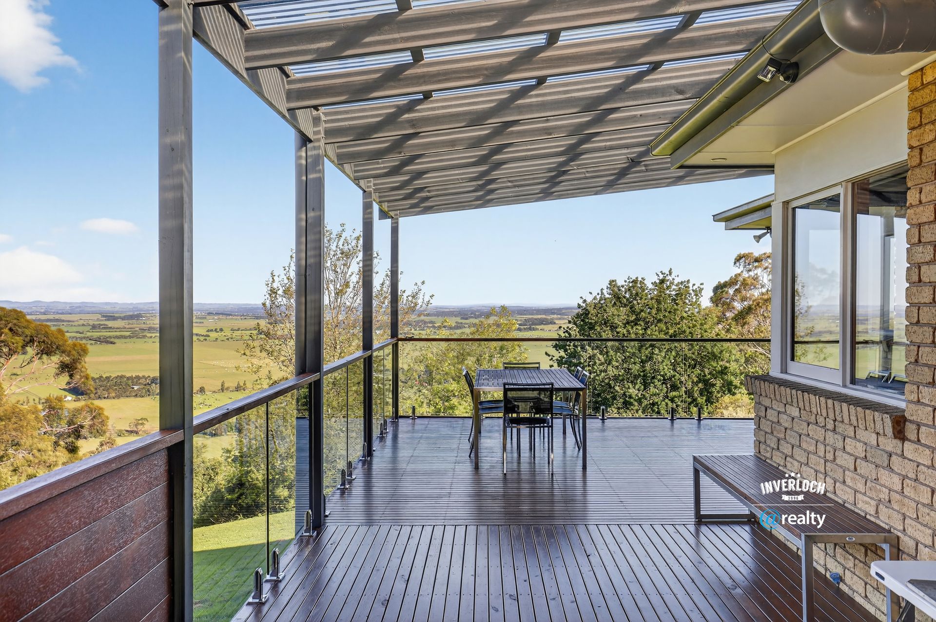 Wooden deck with view of fields and sky, shaded by a pergola.