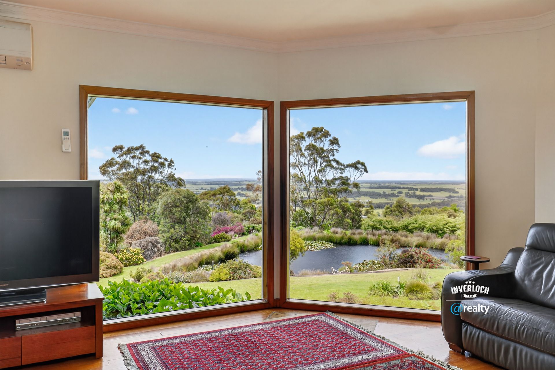 Living room with corner windows overlooking a pond and fields. TV, rug, and black leather chair are present.