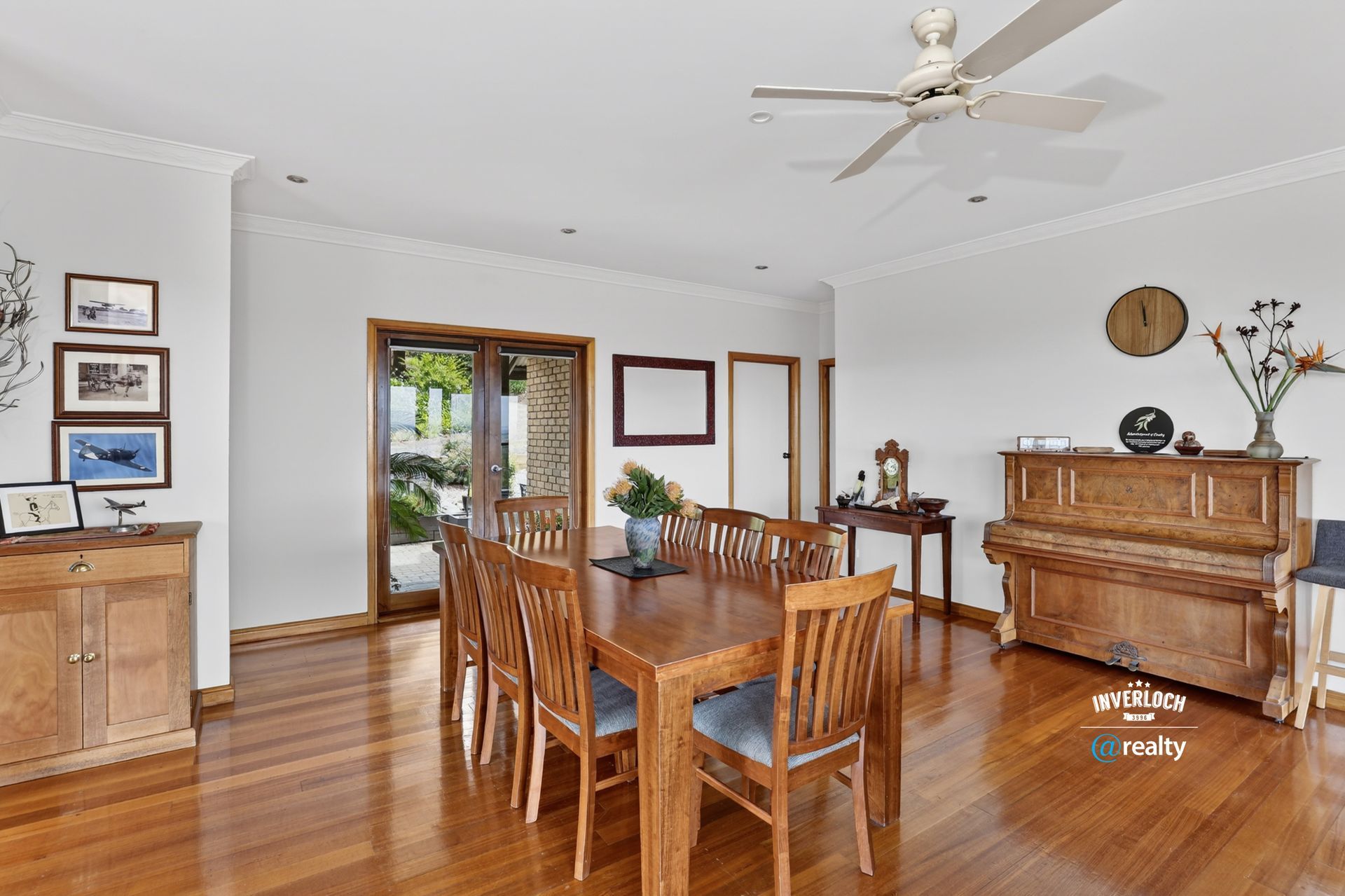 Dining room with wooden table and chairs, piano, and art on the walls, bright and airy.