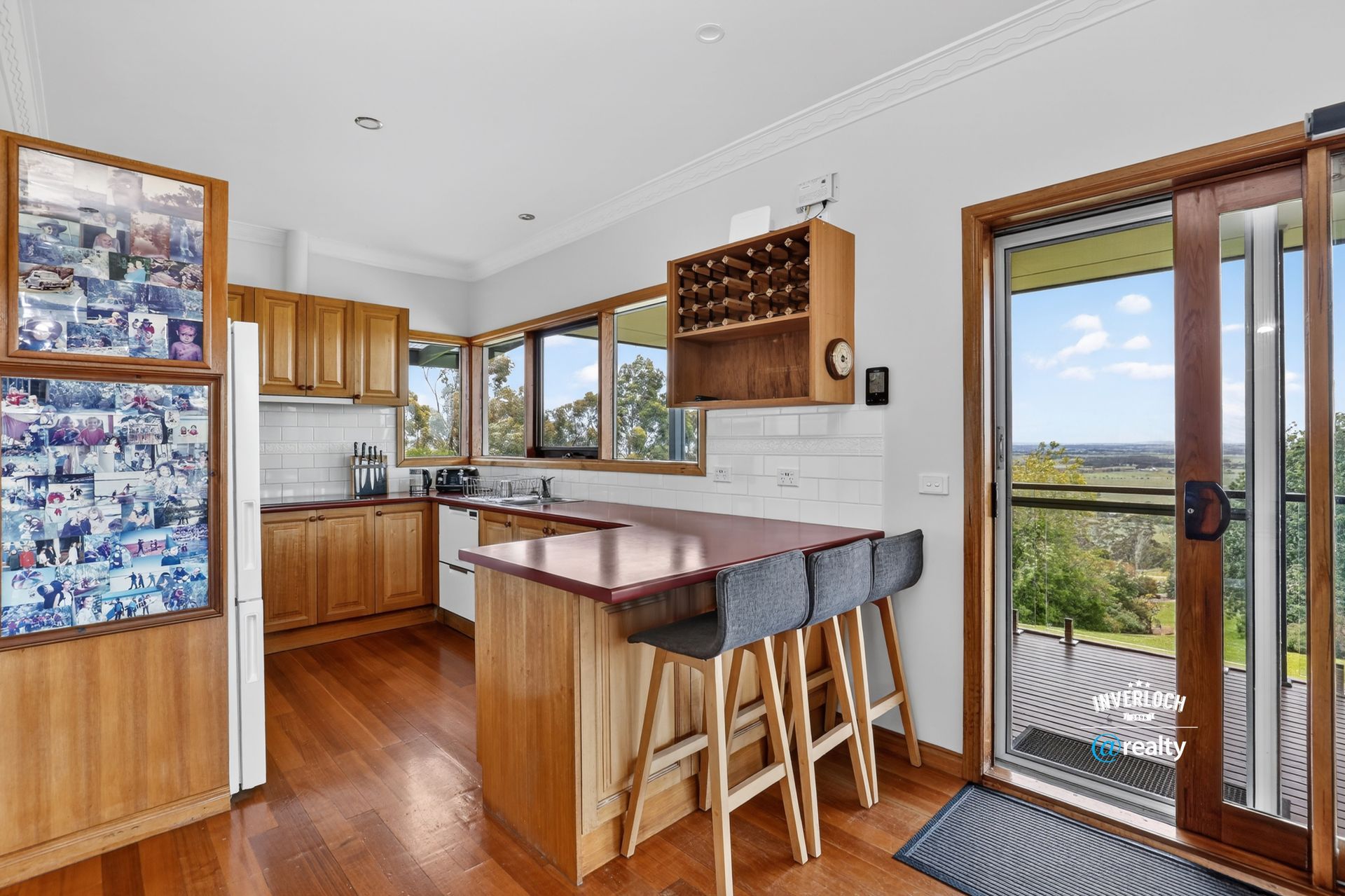 Kitchen with wooden cabinets, red countertop, and stools. Sliding door leads to a view.