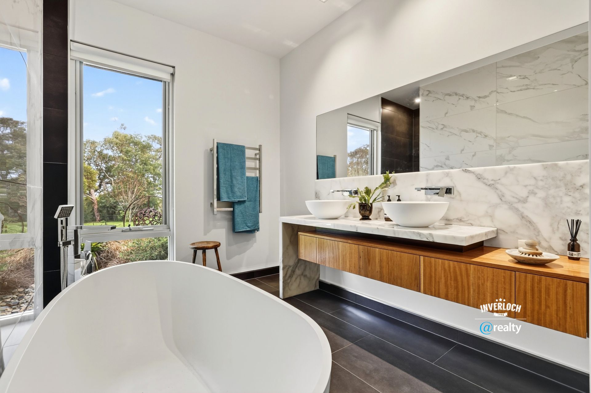 Modern bathroom with a white tub, wooden vanity, and large window overlooking trees.