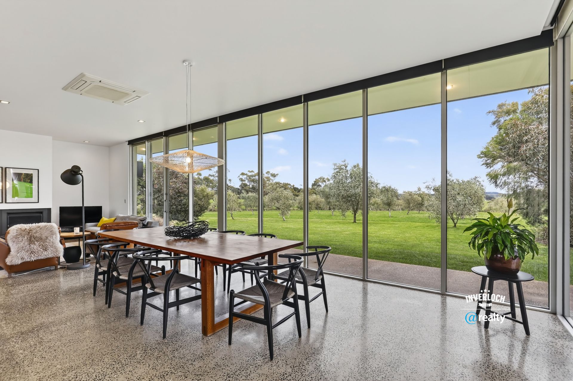 Spacious dining room with large windows overlooking a green field. A long wooden table with chairs is in the center.