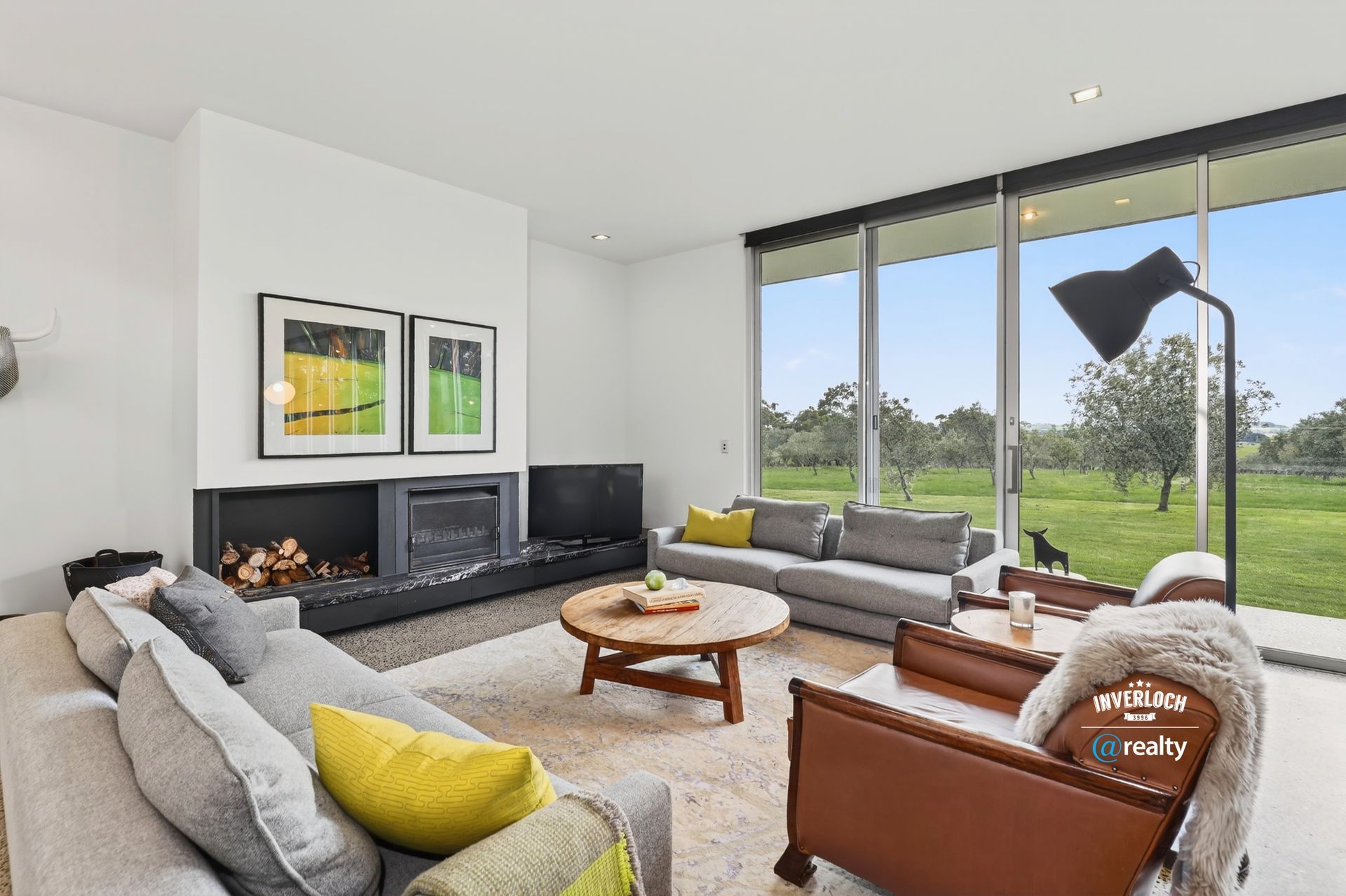 Modern living room with fireplace, sofas, large window overlooking a field, and a black floor lamp.