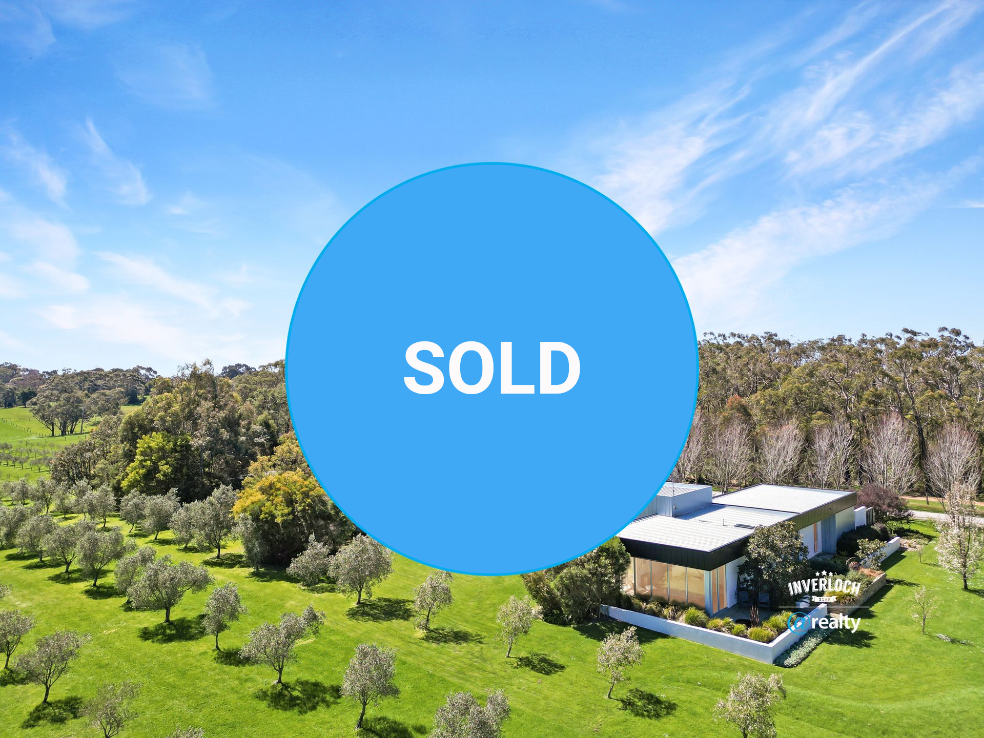 A modern house on a green field with trees, under a blue sky, with an 