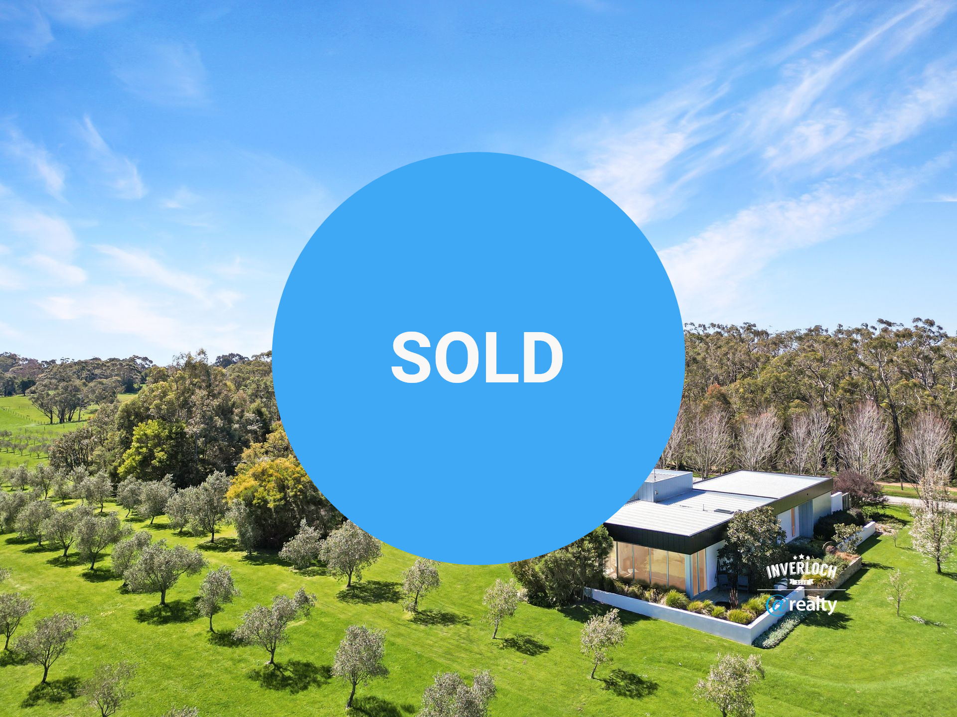 Modern house in a green field with trees, under a bright blue sky.