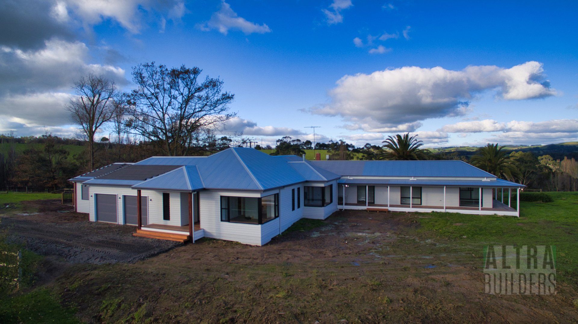 A large white house with a blue roof is sitting in the middle of a grassy field.