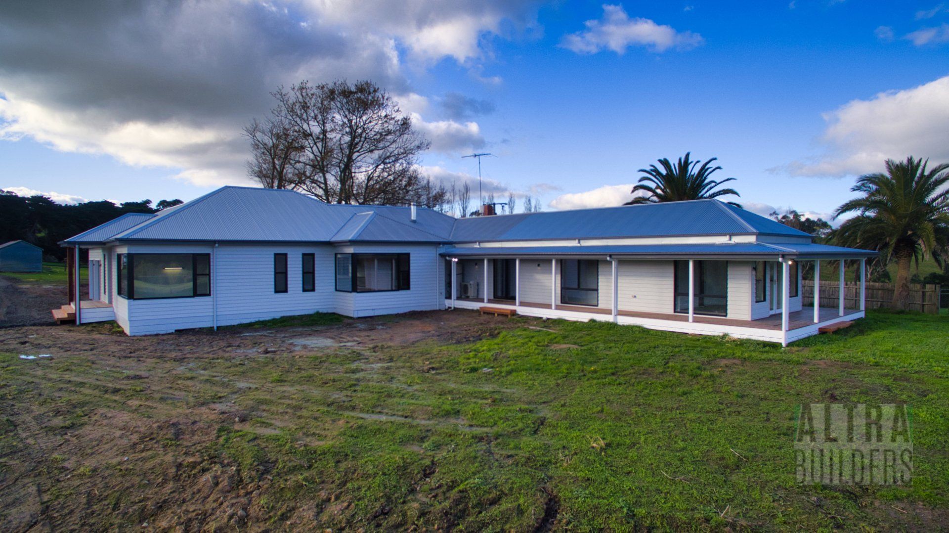A large white house with a porch is sitting in the middle of a grassy field.