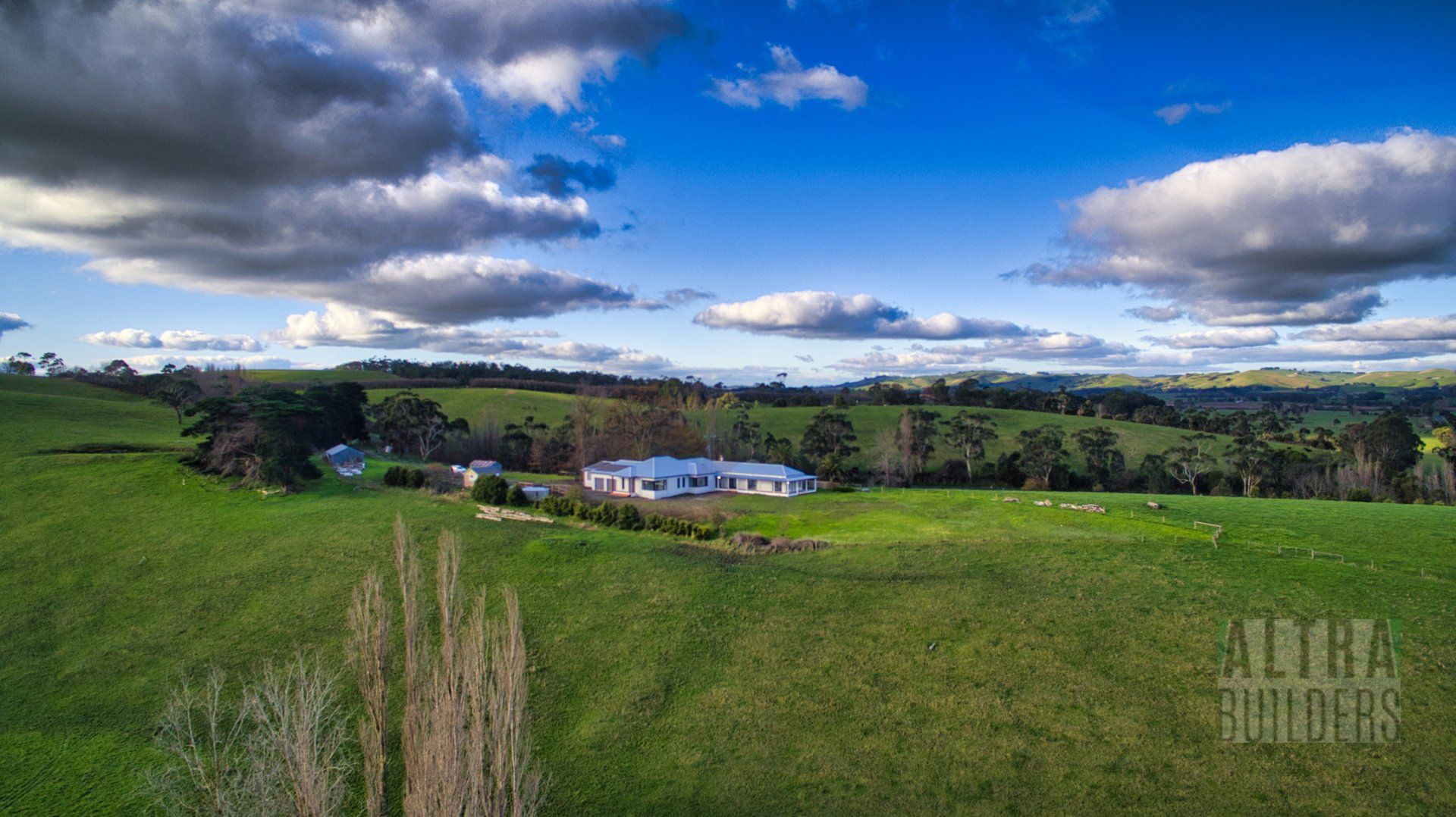 An aerial view of a lush green field with a house in the distance.