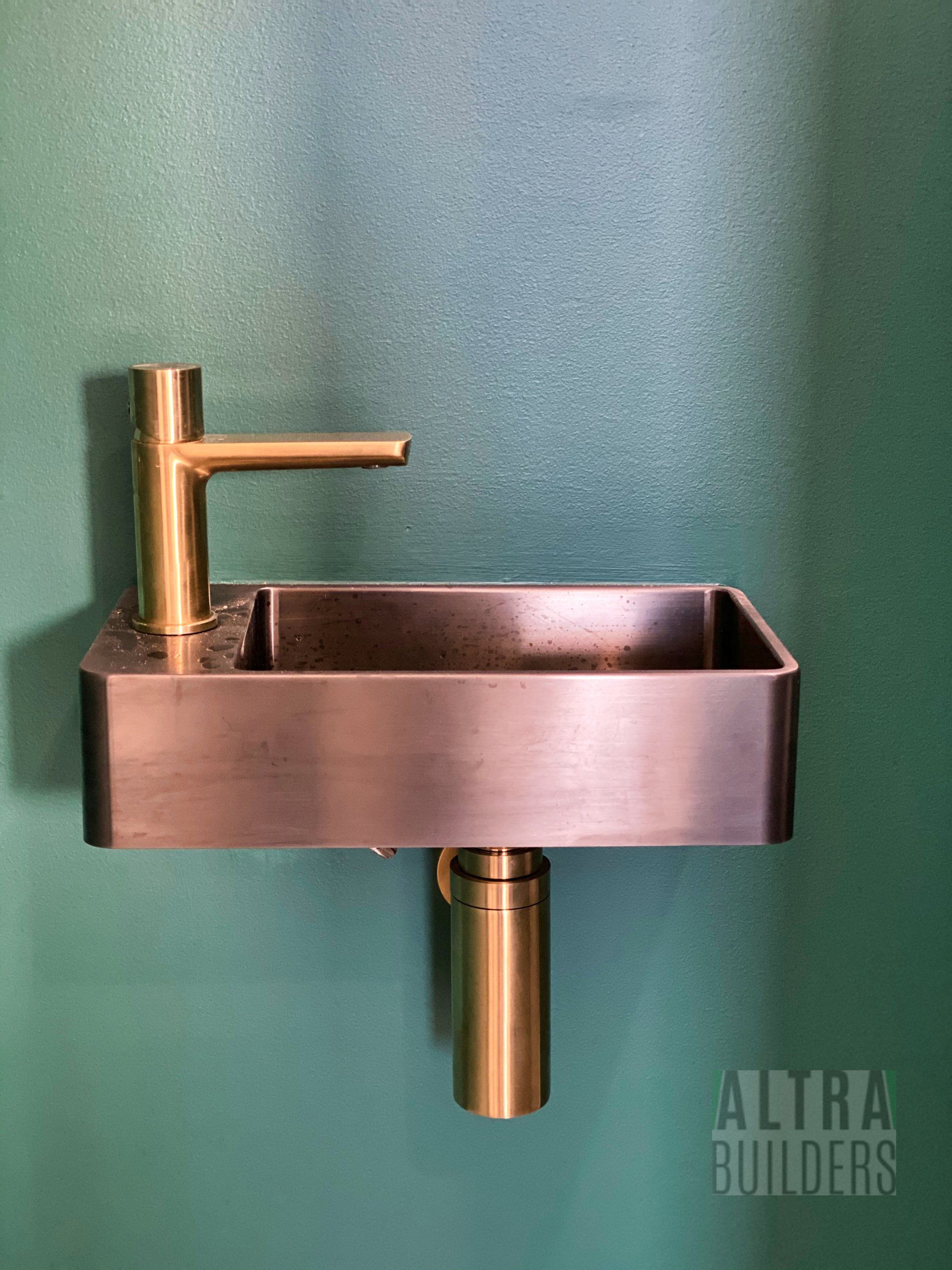 A small copper sink with a faucet on a green wall.