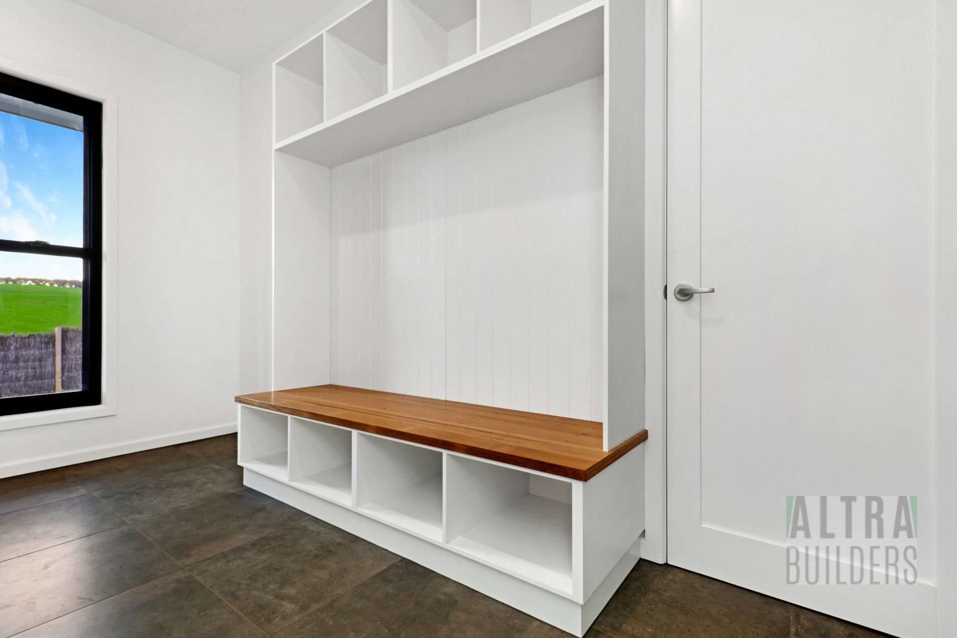 A white shelf with a wooden bench in a room with a window.