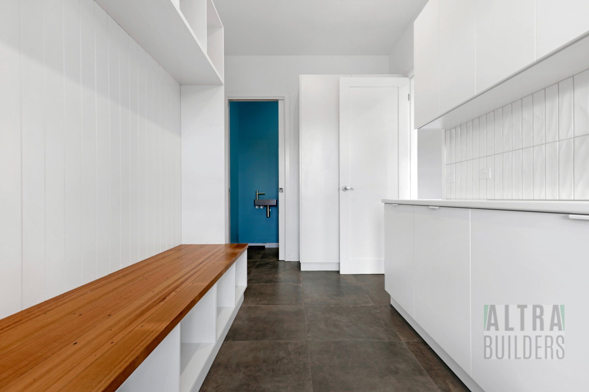 A kitchen with white cabinets and a wooden bench that says altra builders