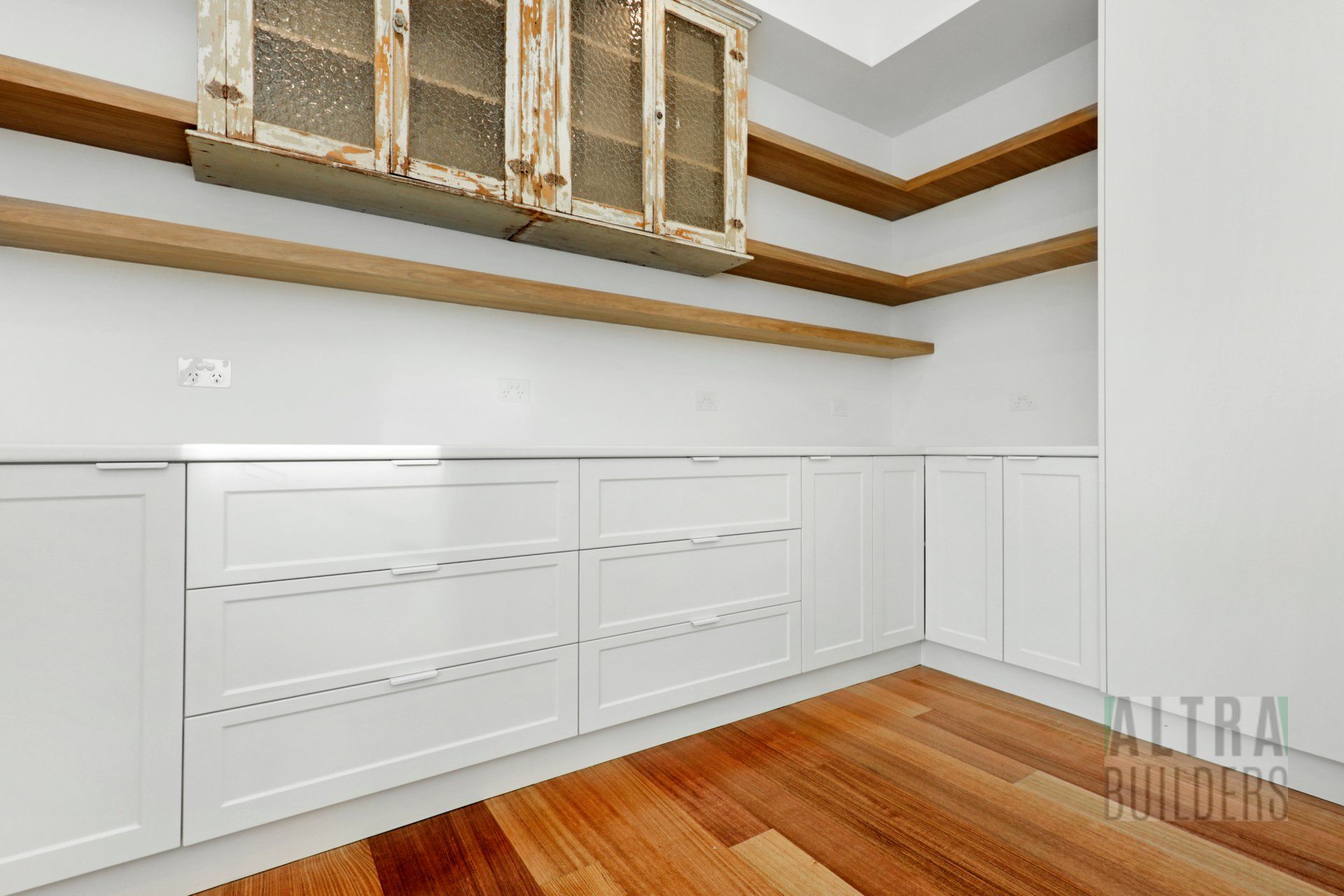 A kitchen with white cabinets and wooden shelves.