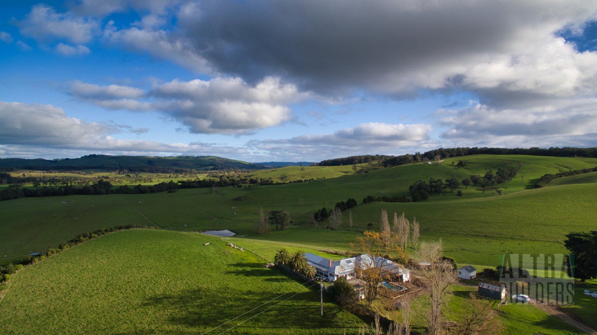 An aerial view of a lush green field with a house in the distance.