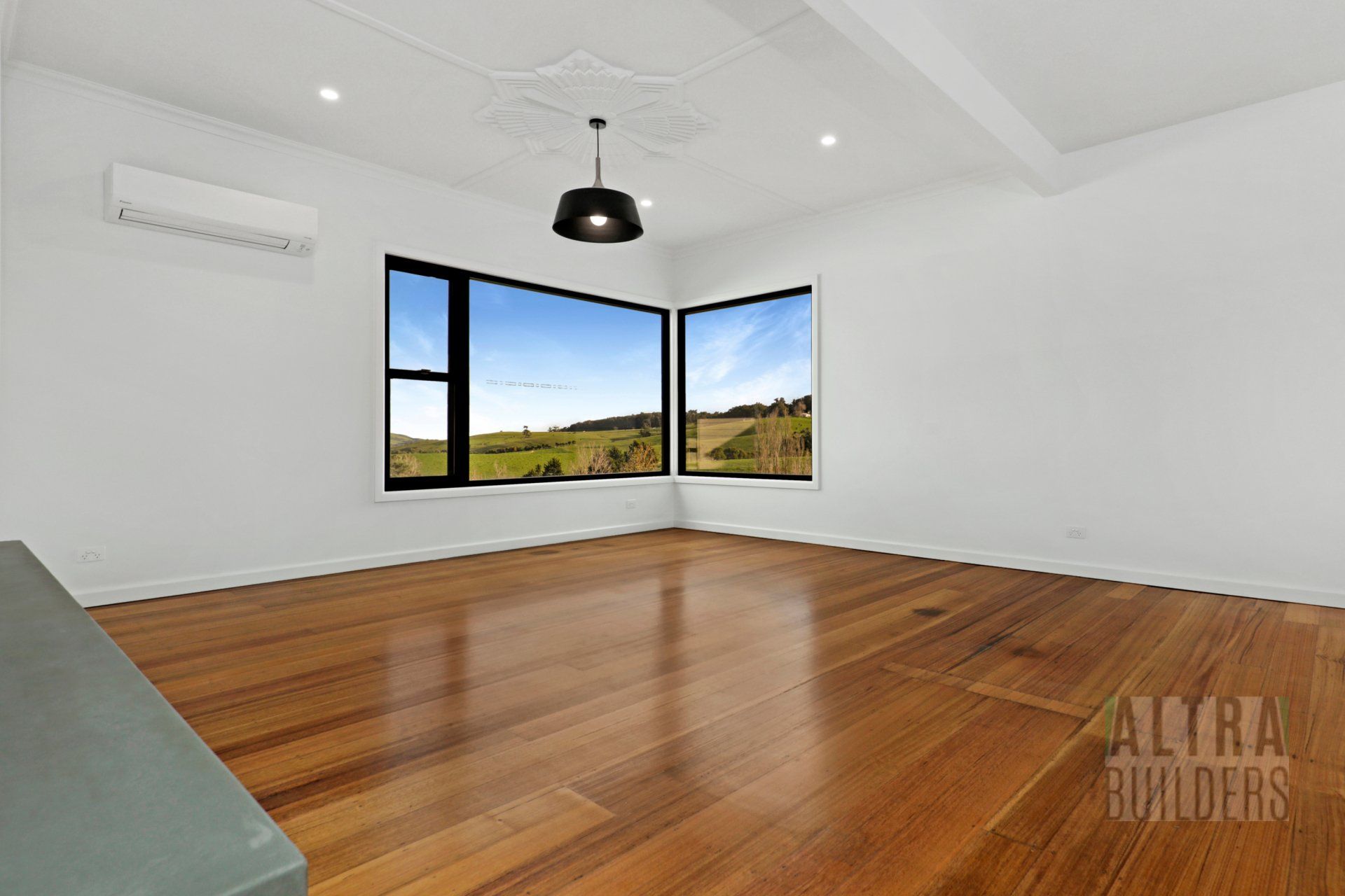 An empty living room with hardwood floors and two windows.