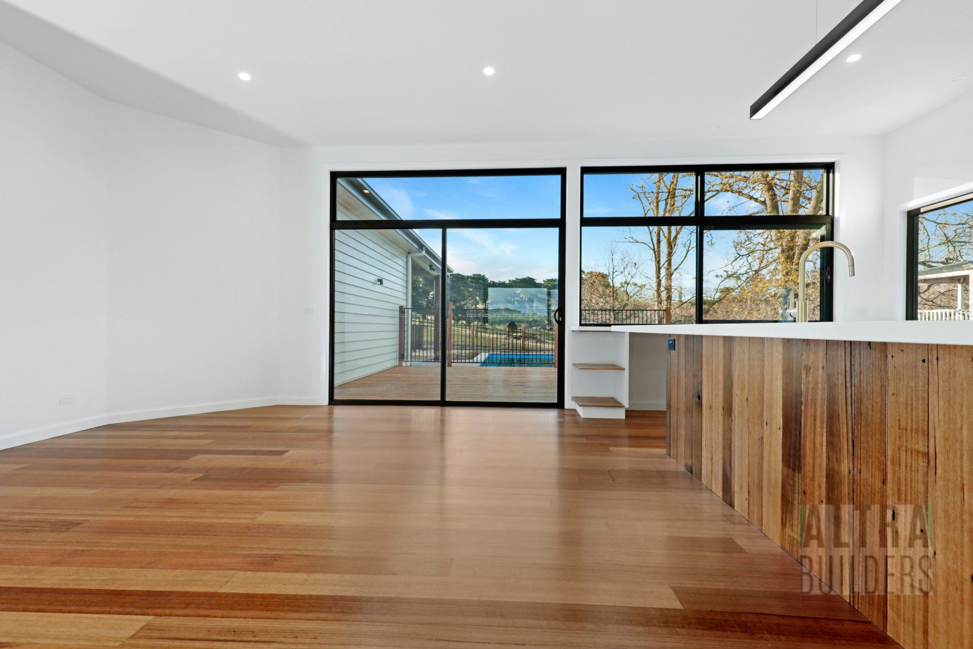 An empty living room with hardwood floors and sliding glass doors leading to a kitchen.