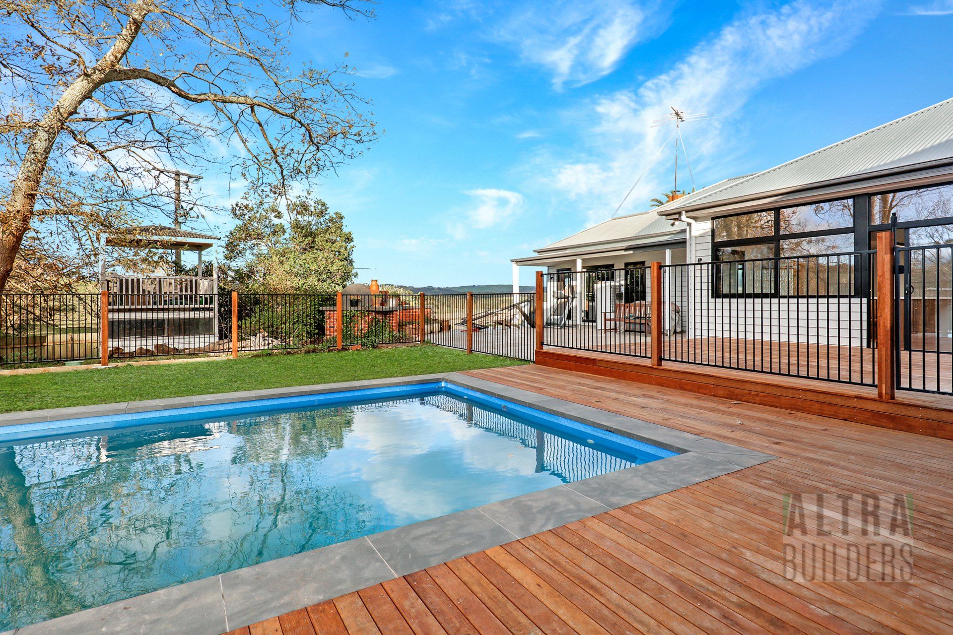 A large swimming pool is surrounded by a wooden deck in front of a house.