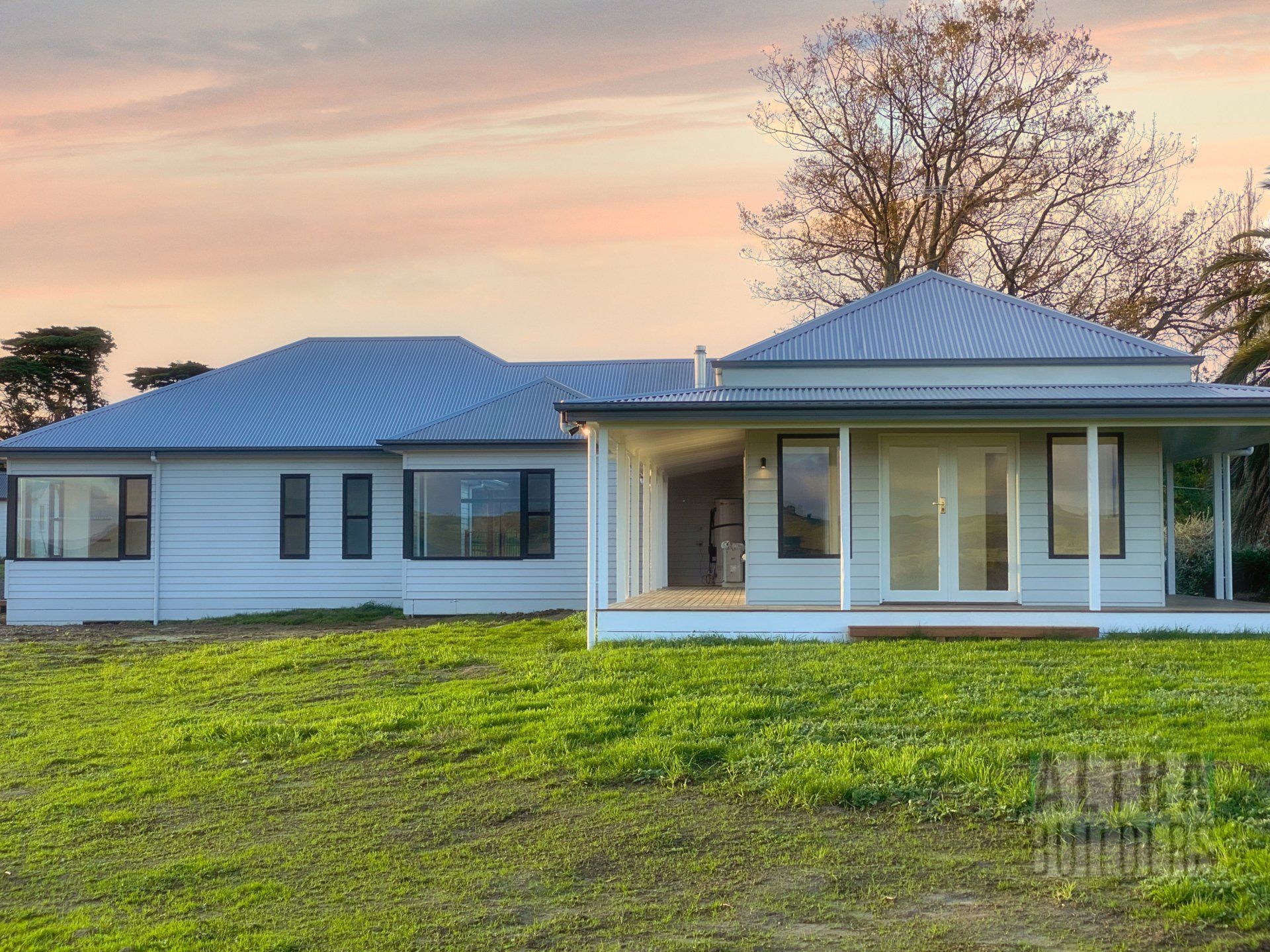 A large white house with a porch is sitting in the middle of a grassy field.