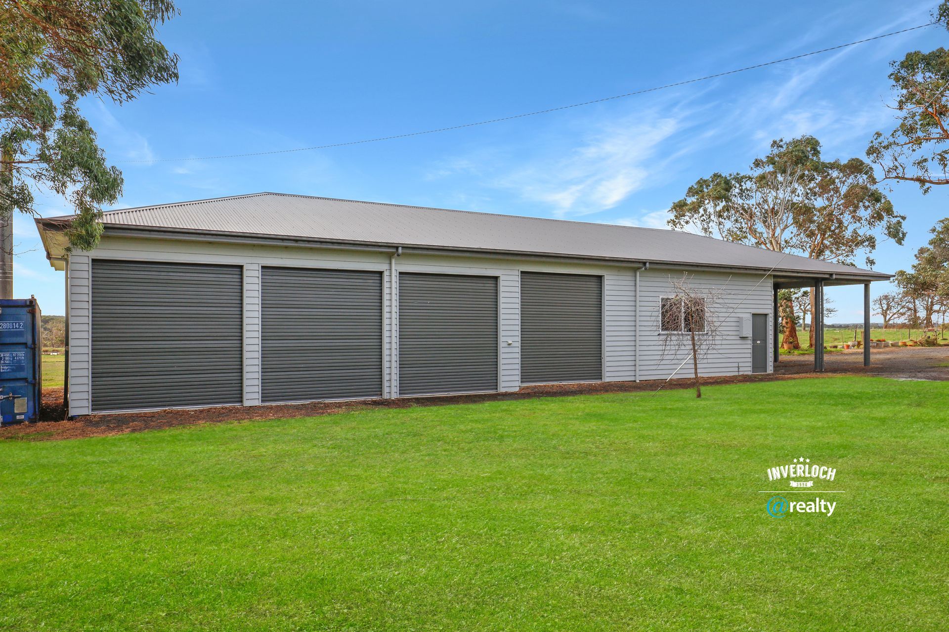 A large building with three garage doors is sitting on top of a lush green field.