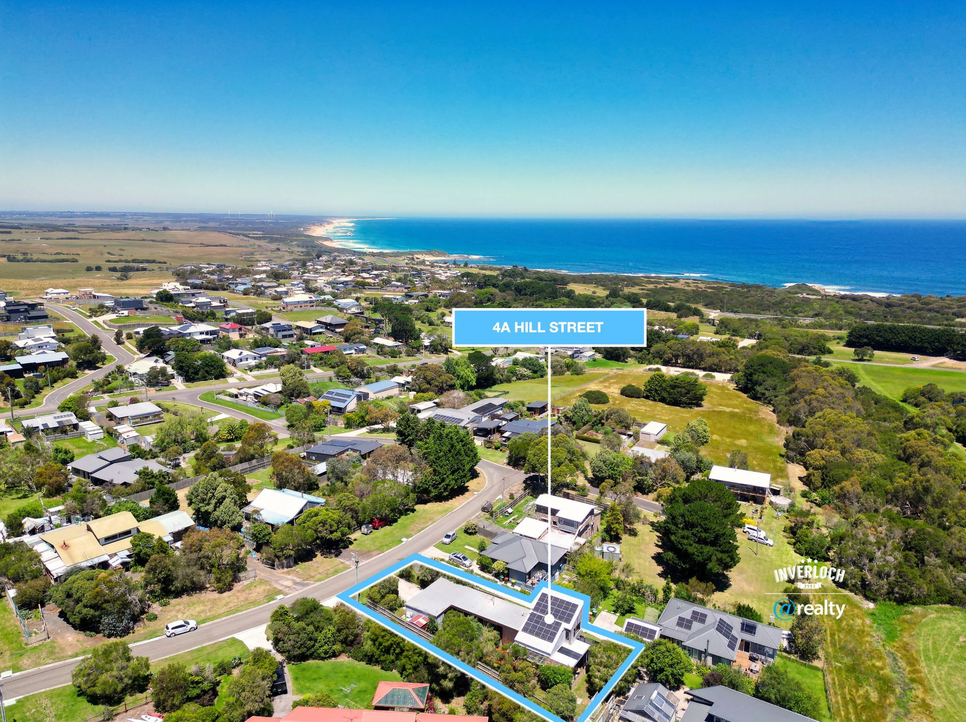 Aerial view of a coastal neighborhood with a blue ocean horizon and a blue sign above a house.