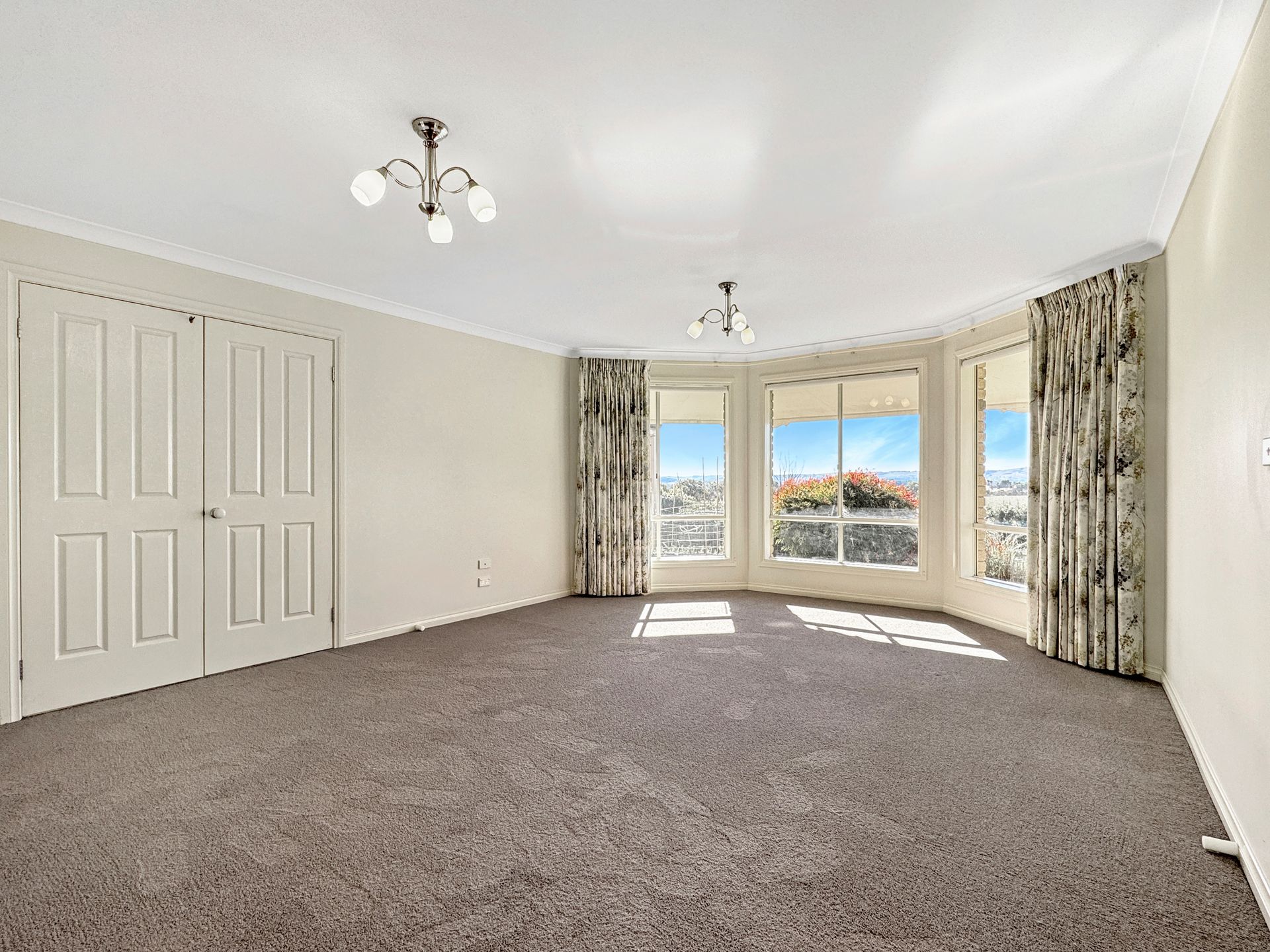 An empty living room with a lot of windows and a chandelier.