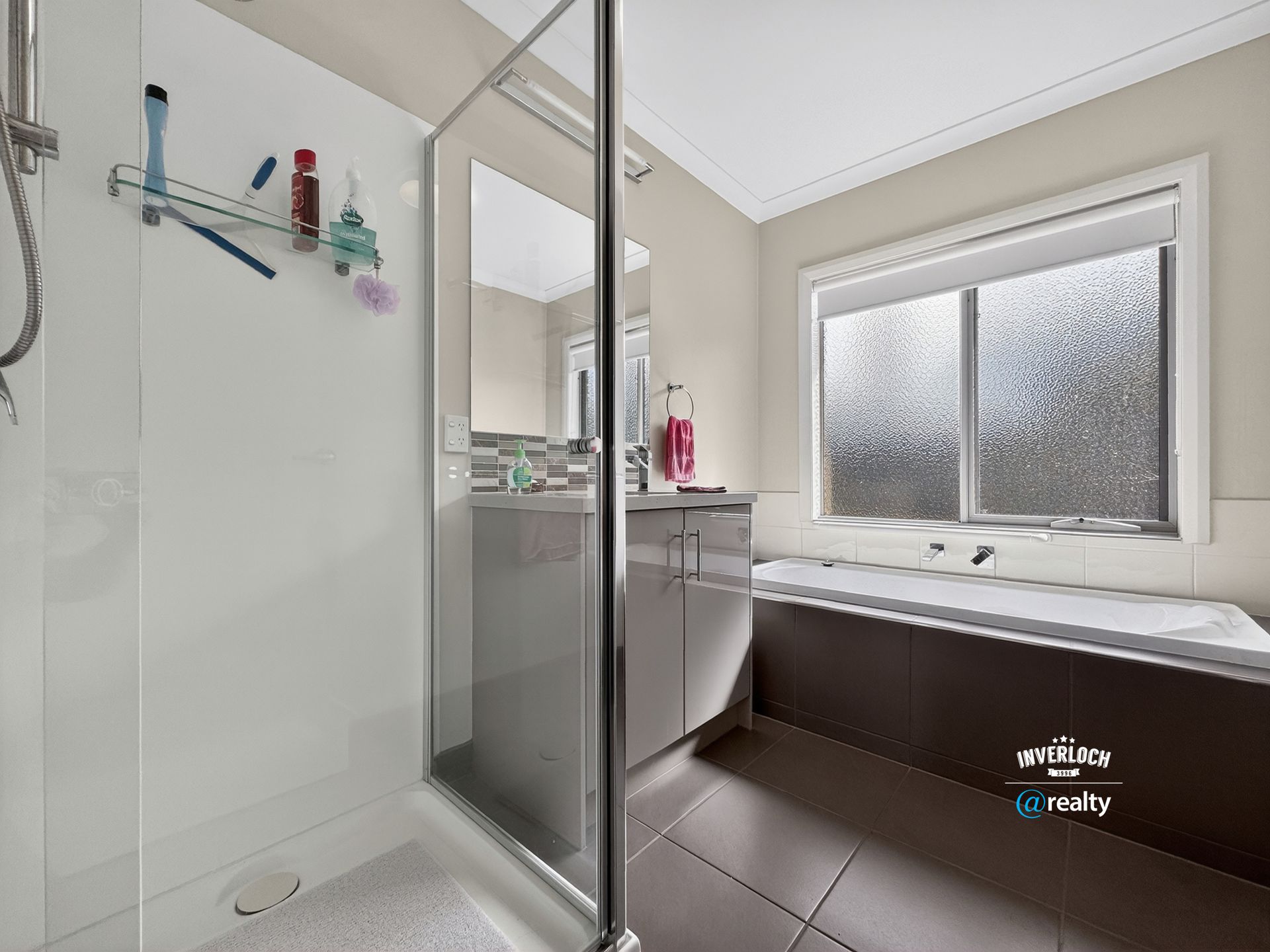 A bright bathroom featuring a walk-in shower with a glass door, a sleek vanity with a mirror, and a window above a tub.