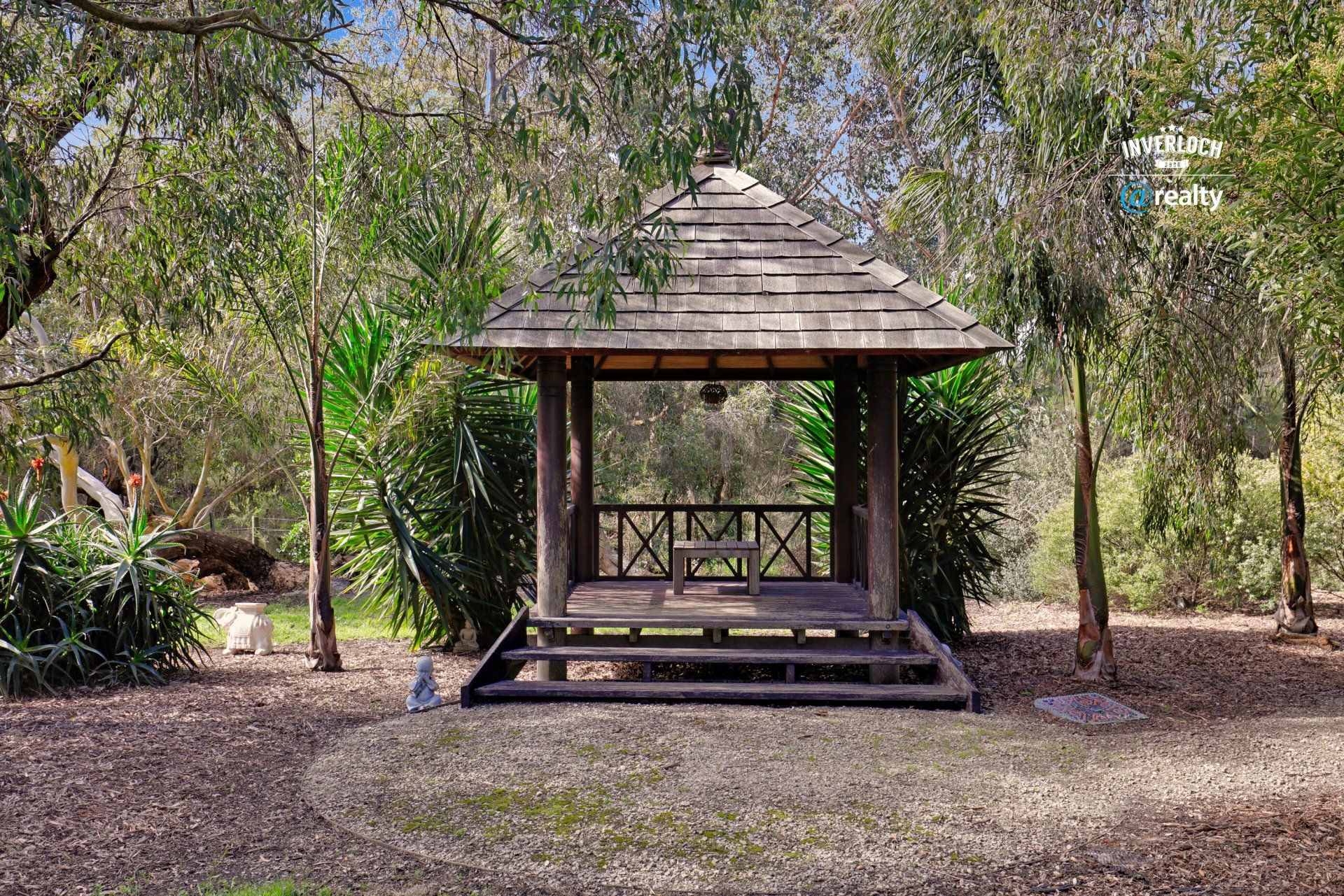 A wooden gazebo in the middle of a forest surrounded by trees.