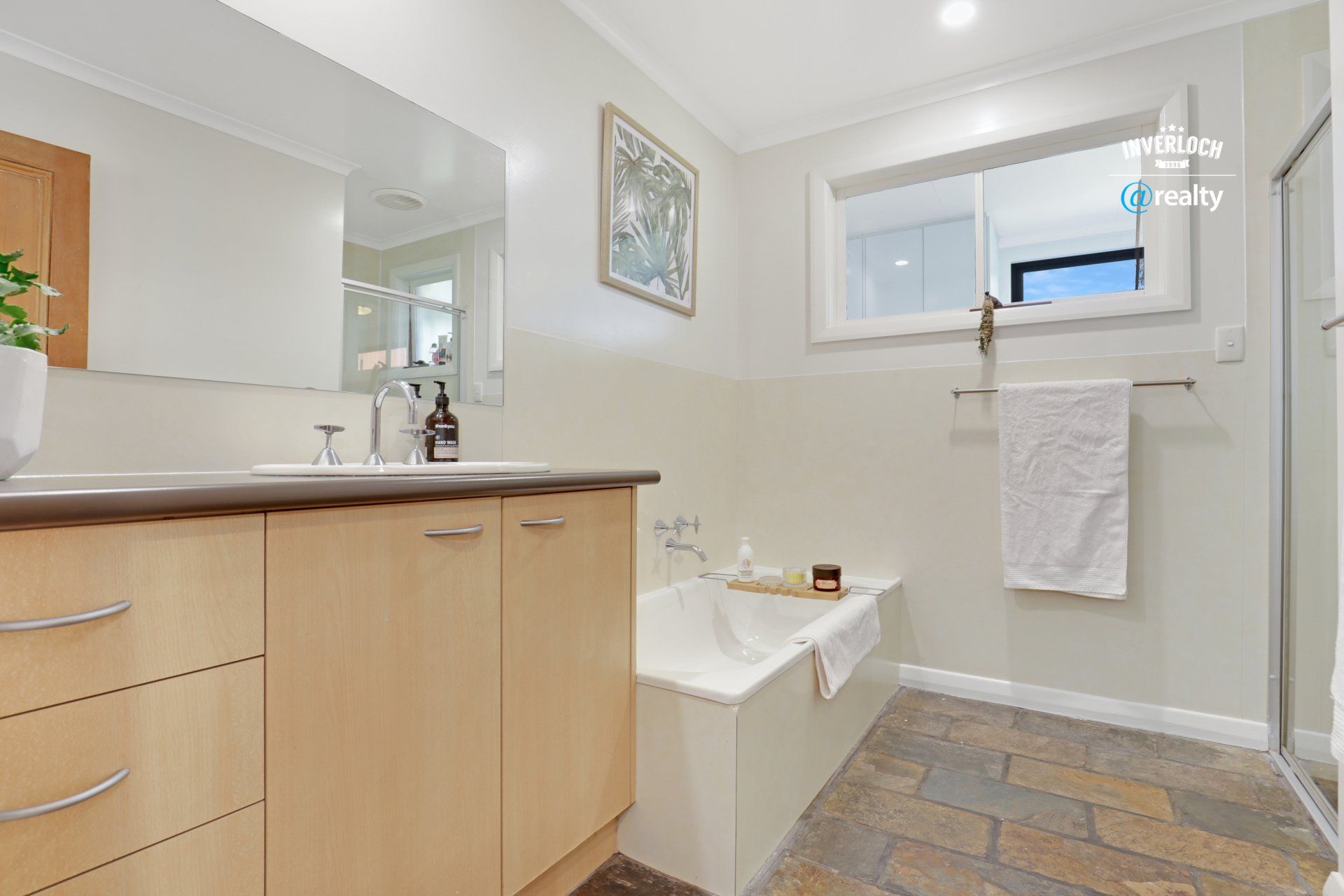 A bathroom with a tub , sink , mirror and window.