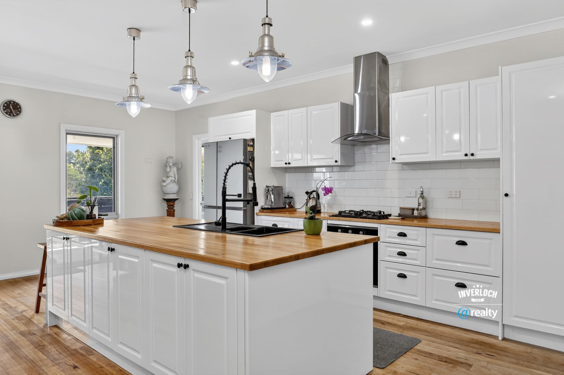 White kitchen with island, wooden countertops, stainless steel appliances, pendant lights.