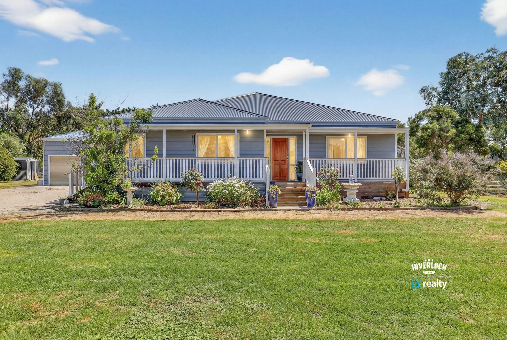 Blue and white house with a porch and green lawn, under a blue sky.