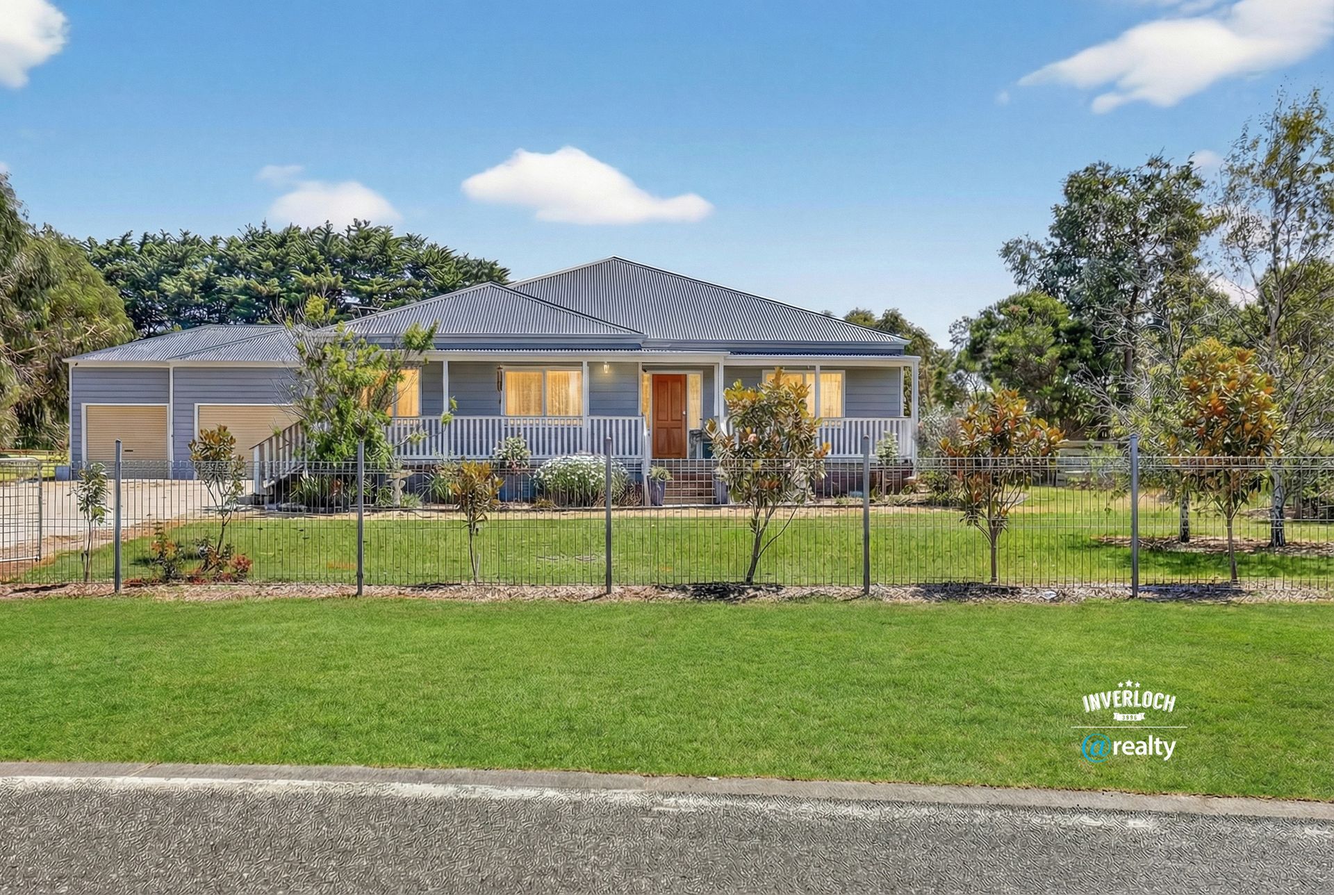 Single-story modern house with a fenced front yard and green lawn under a blue sky