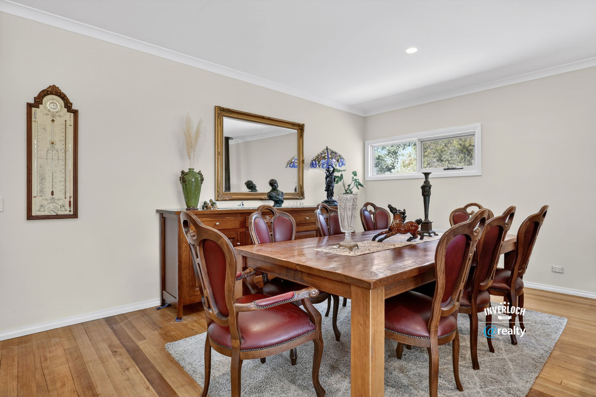 Dining room with wooden table and chairs, buffet, mirror, and hardwood floors.