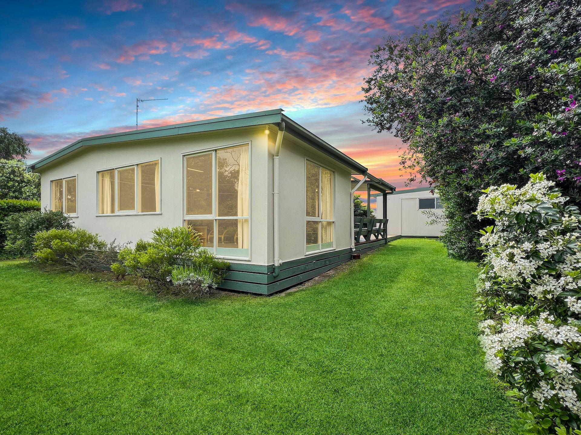 A small white house is sitting on top of a lush green lawn.