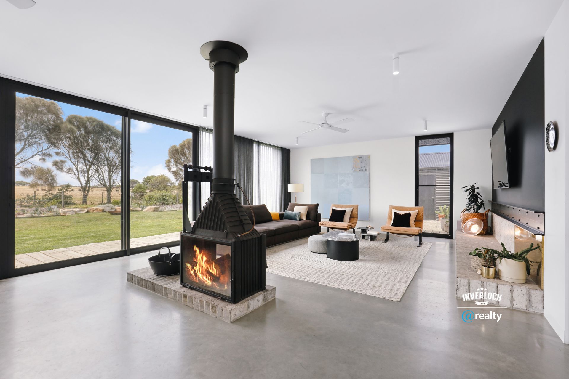 Living room with fireplace, windows overlooking a grassy field, modern decor.