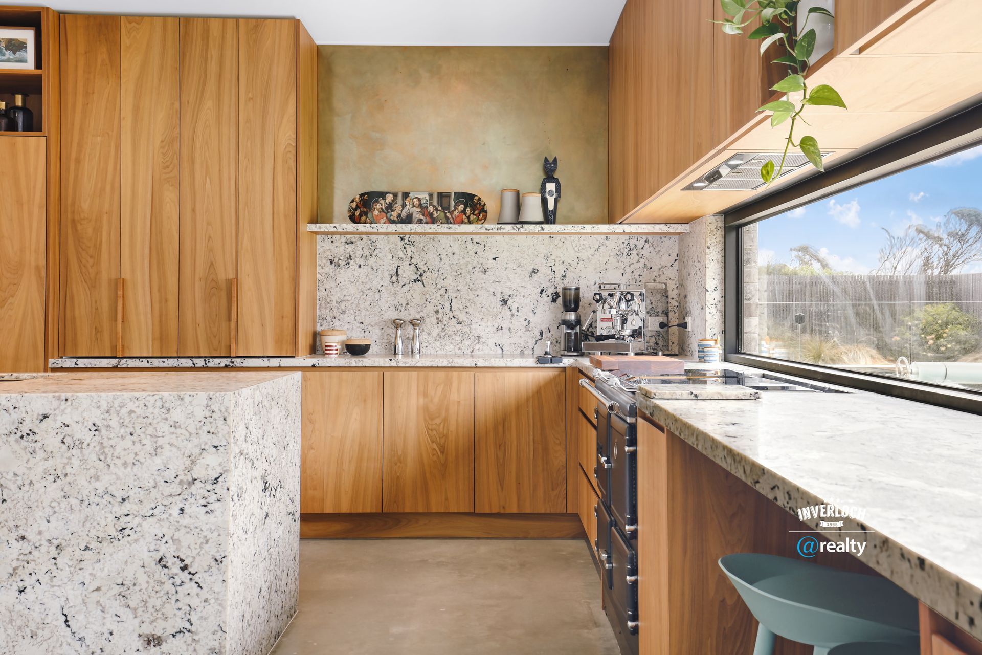 Kitchen with light wood cabinets, speckled countertops, and a long window.