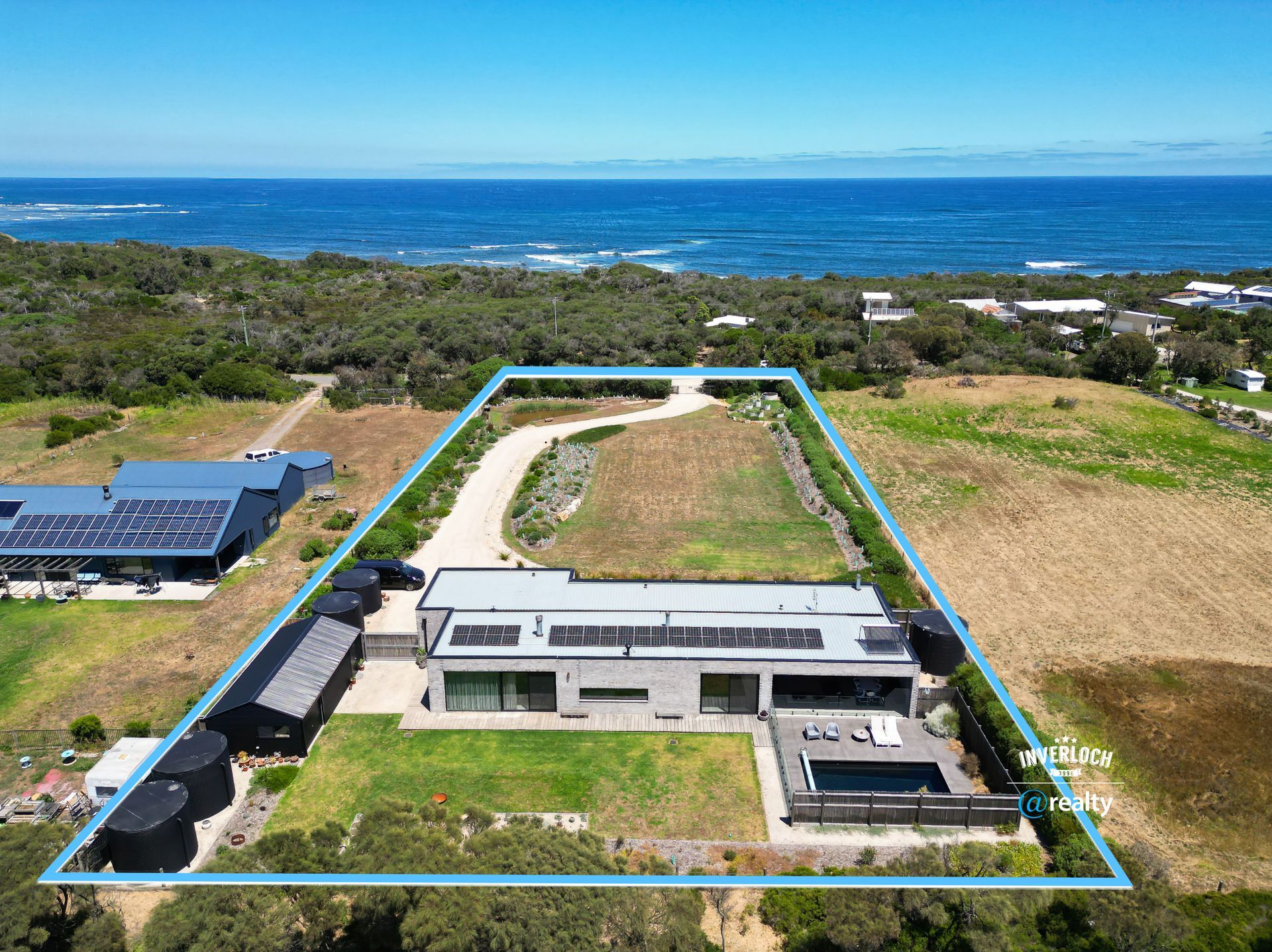 Aerial view of a modern house with a pool, ocean in background. Property outlined in blue.