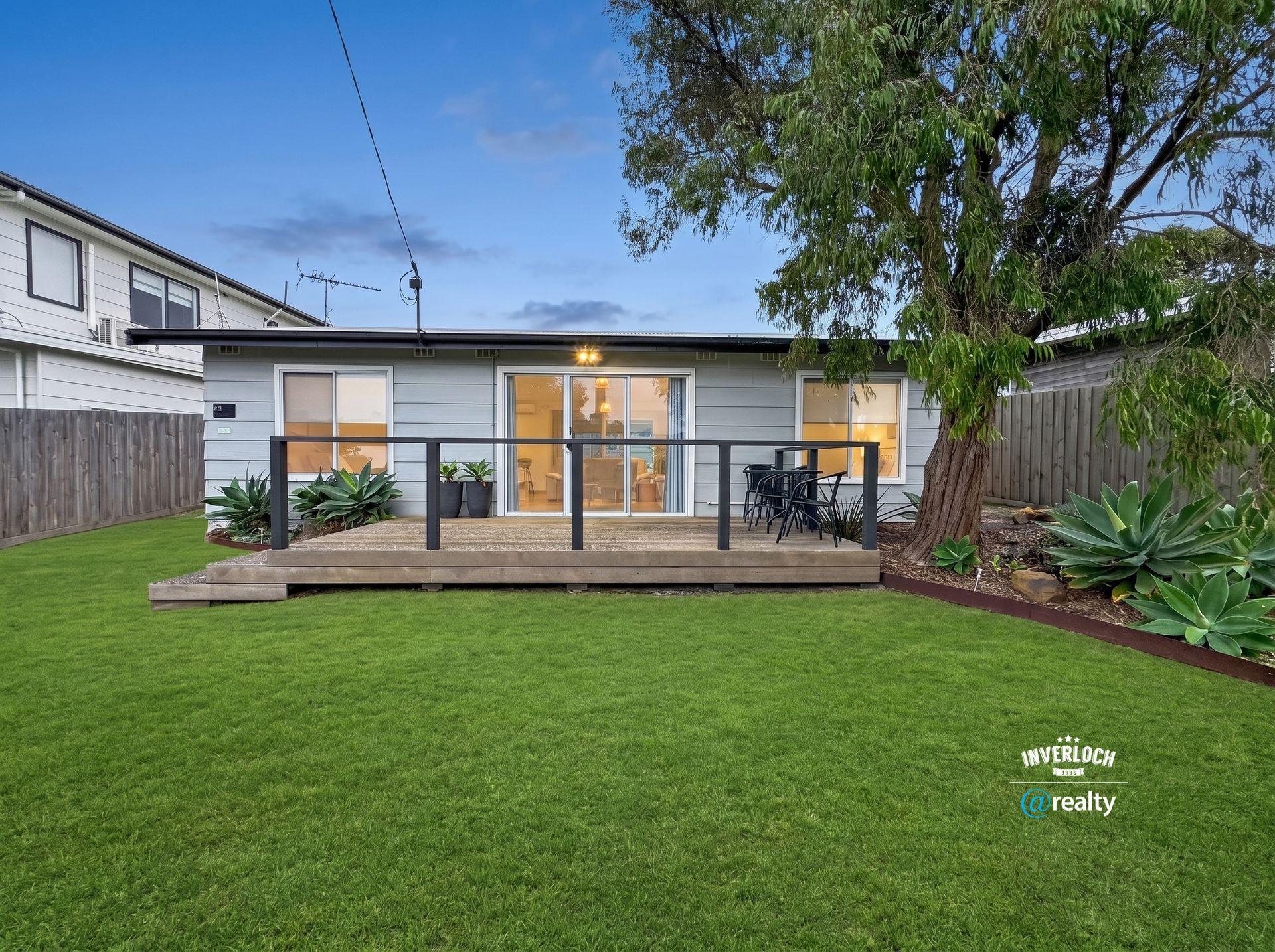 Backyard with a modern house, large green lawn, wooden deck, and sliding glass doors at dusk