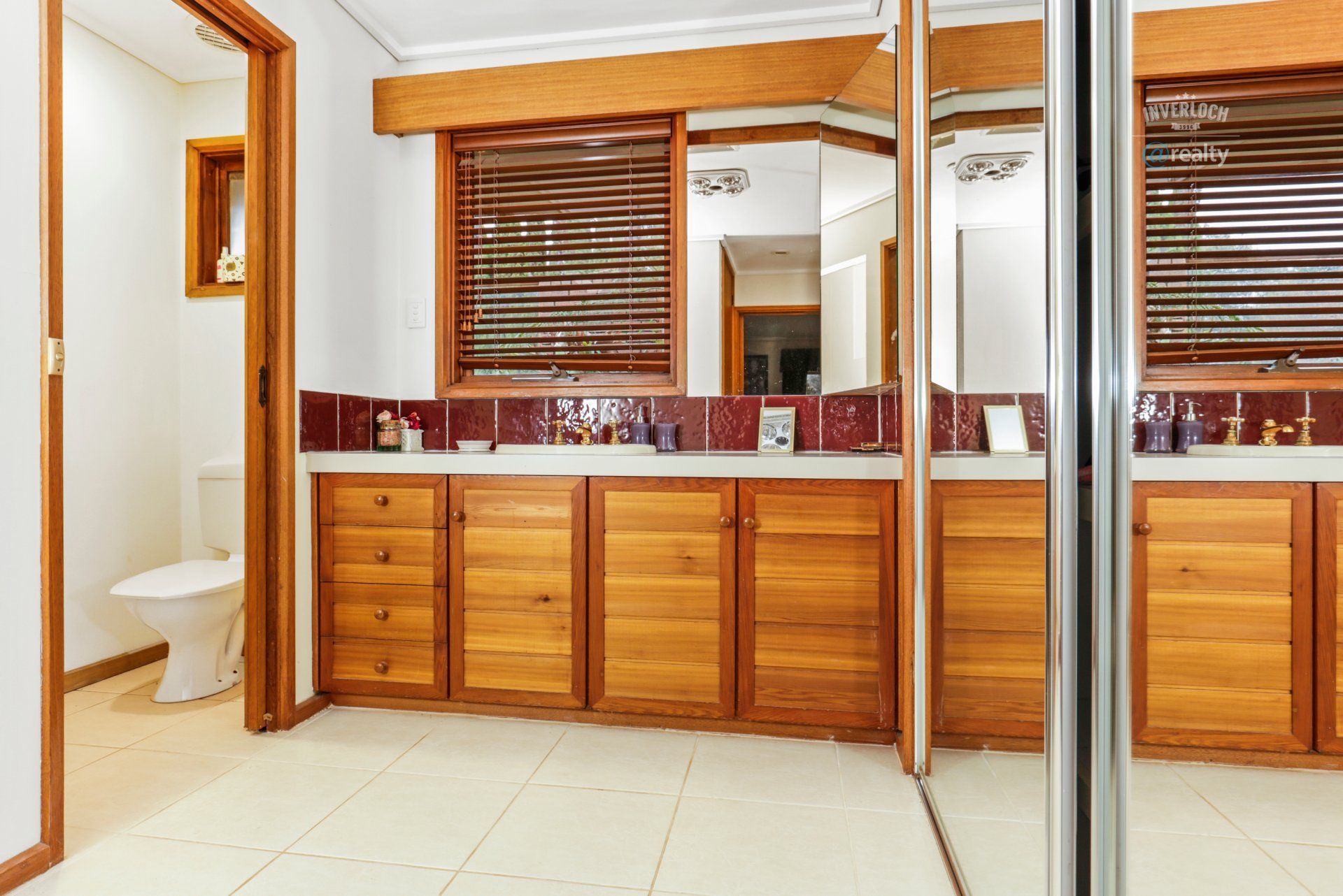 A bathroom with wooden cabinets , a toilet , and a large mirror.