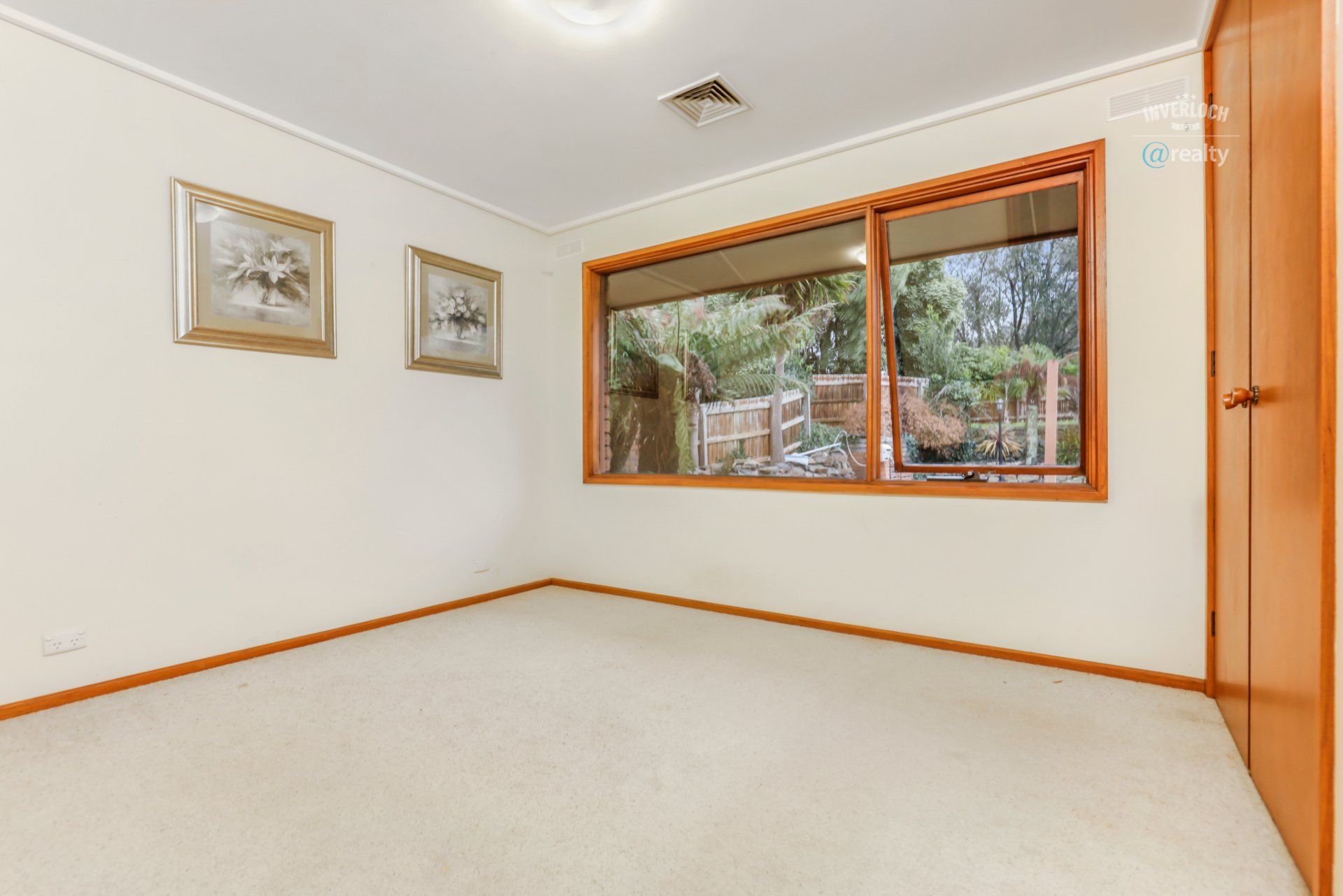 An empty room with a large window and two paintings on the wall.