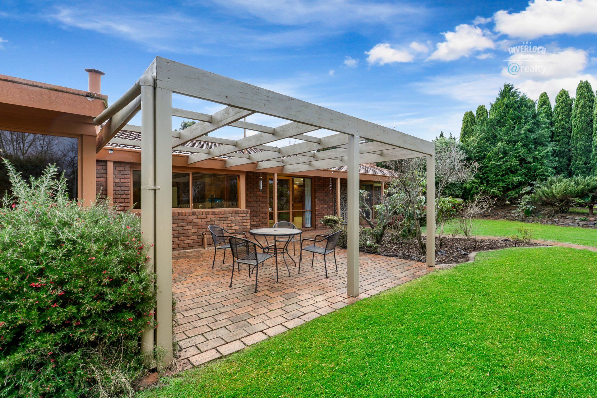 A patio with a table and chairs under a pergola in the backyard of a house.