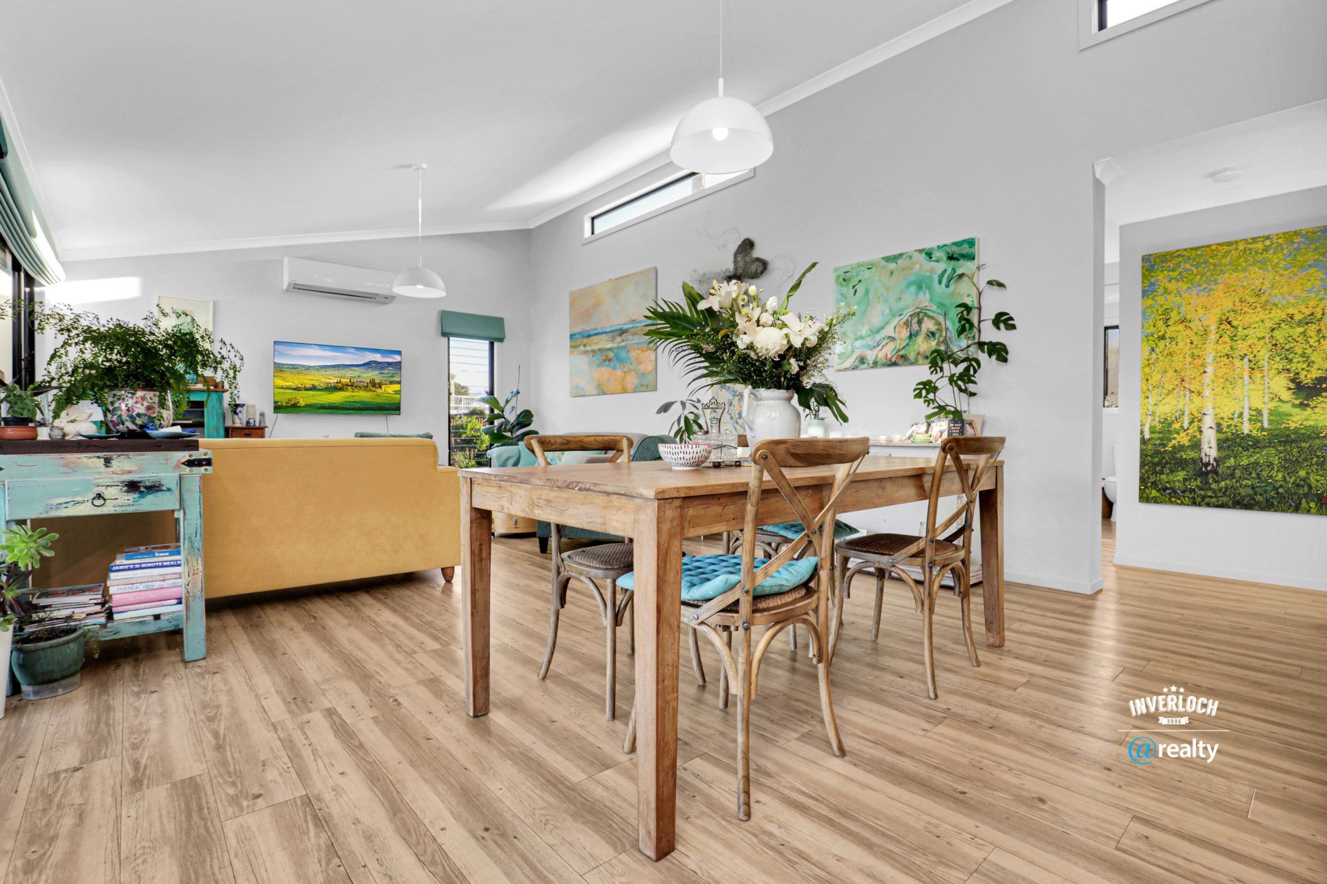 A dining room with a wooden table and chairs and paintings on the wall.