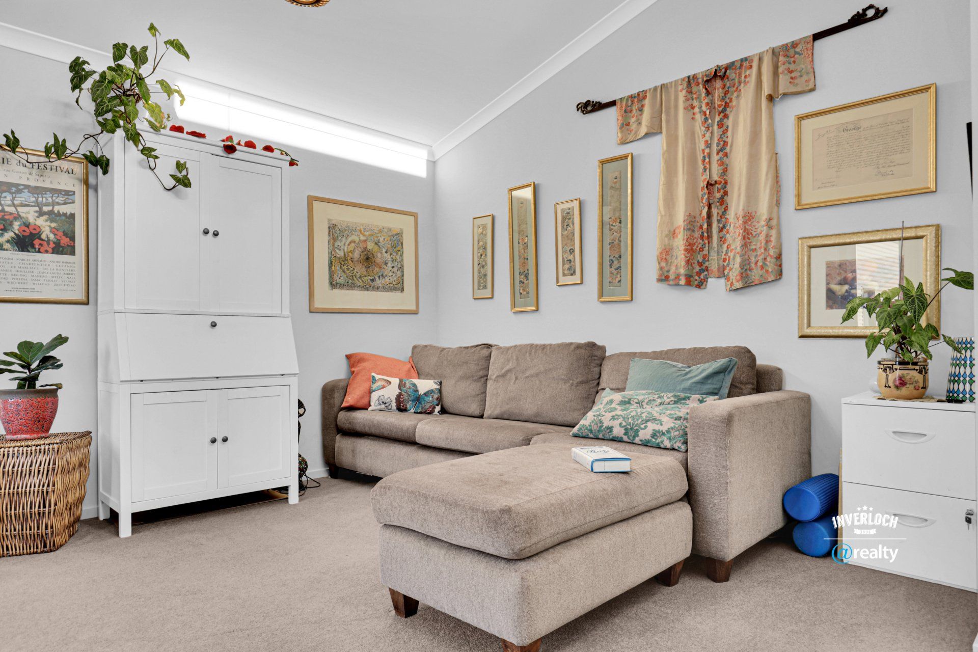 A living room with a couch , ottoman , dresser and pictures on the wall.