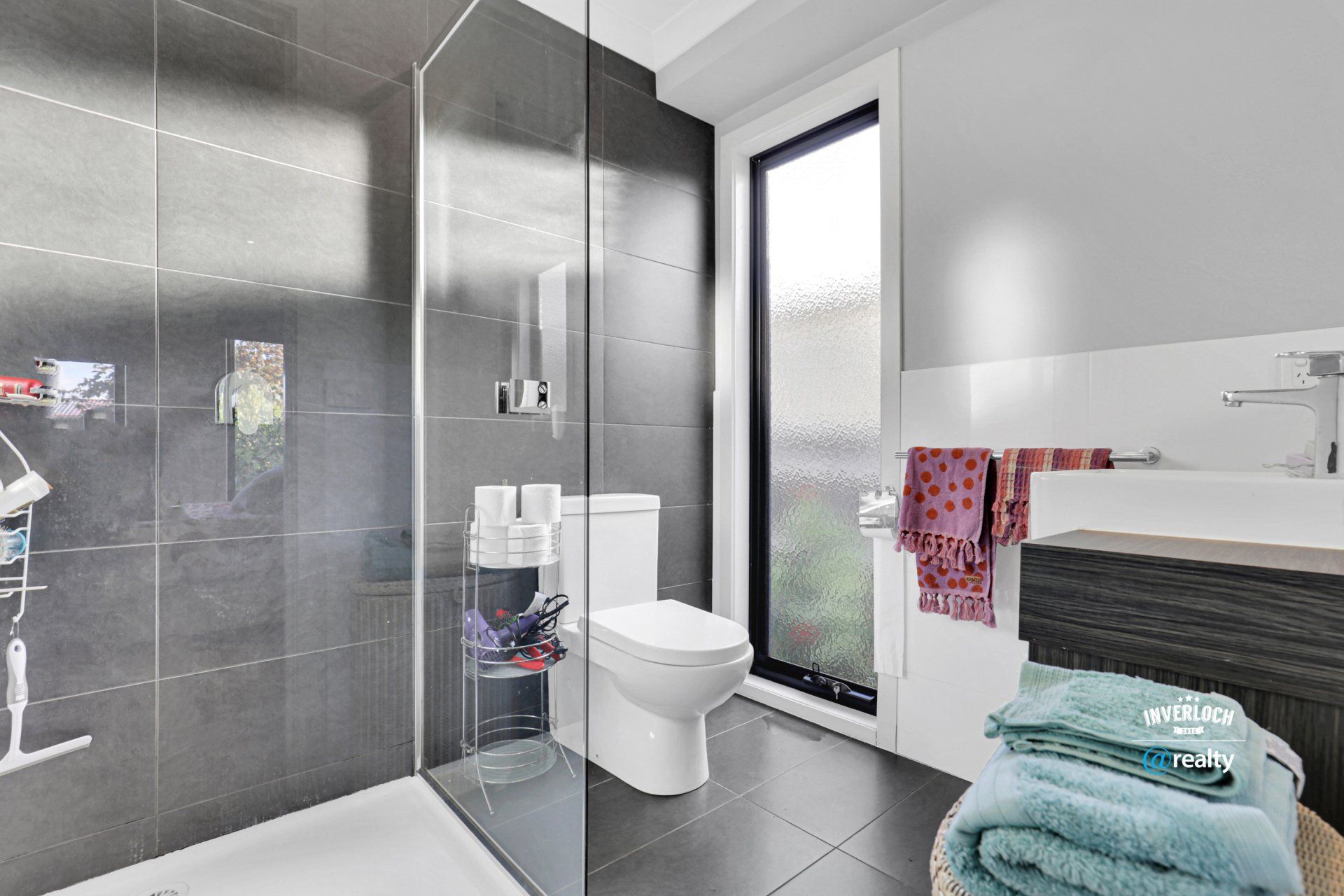 A bathroom with a toilet , sink , shower and window.