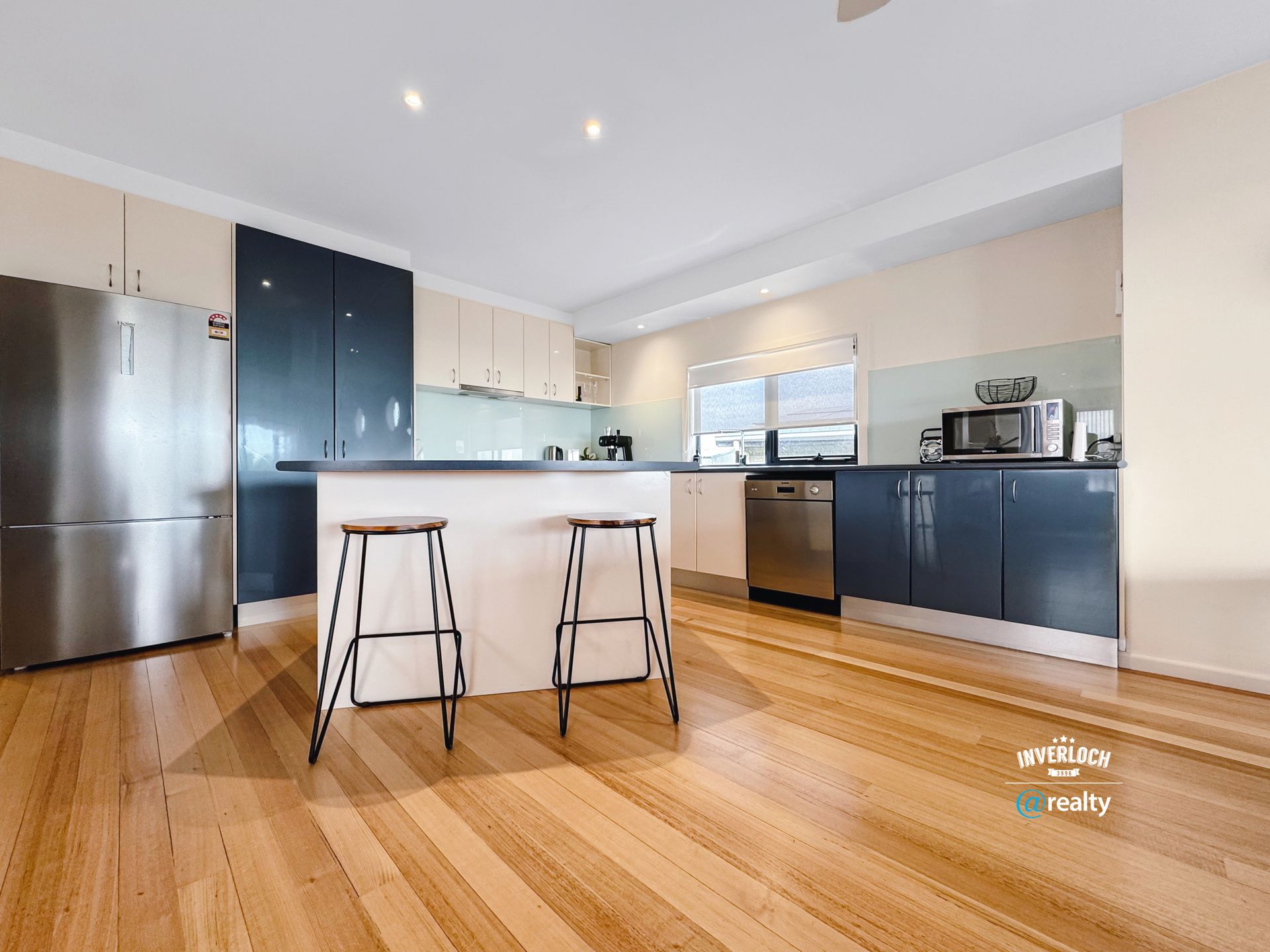 Modern kitchen with stainless steel appliances, dark blue cabinets, light wood floor, and island with stools.
