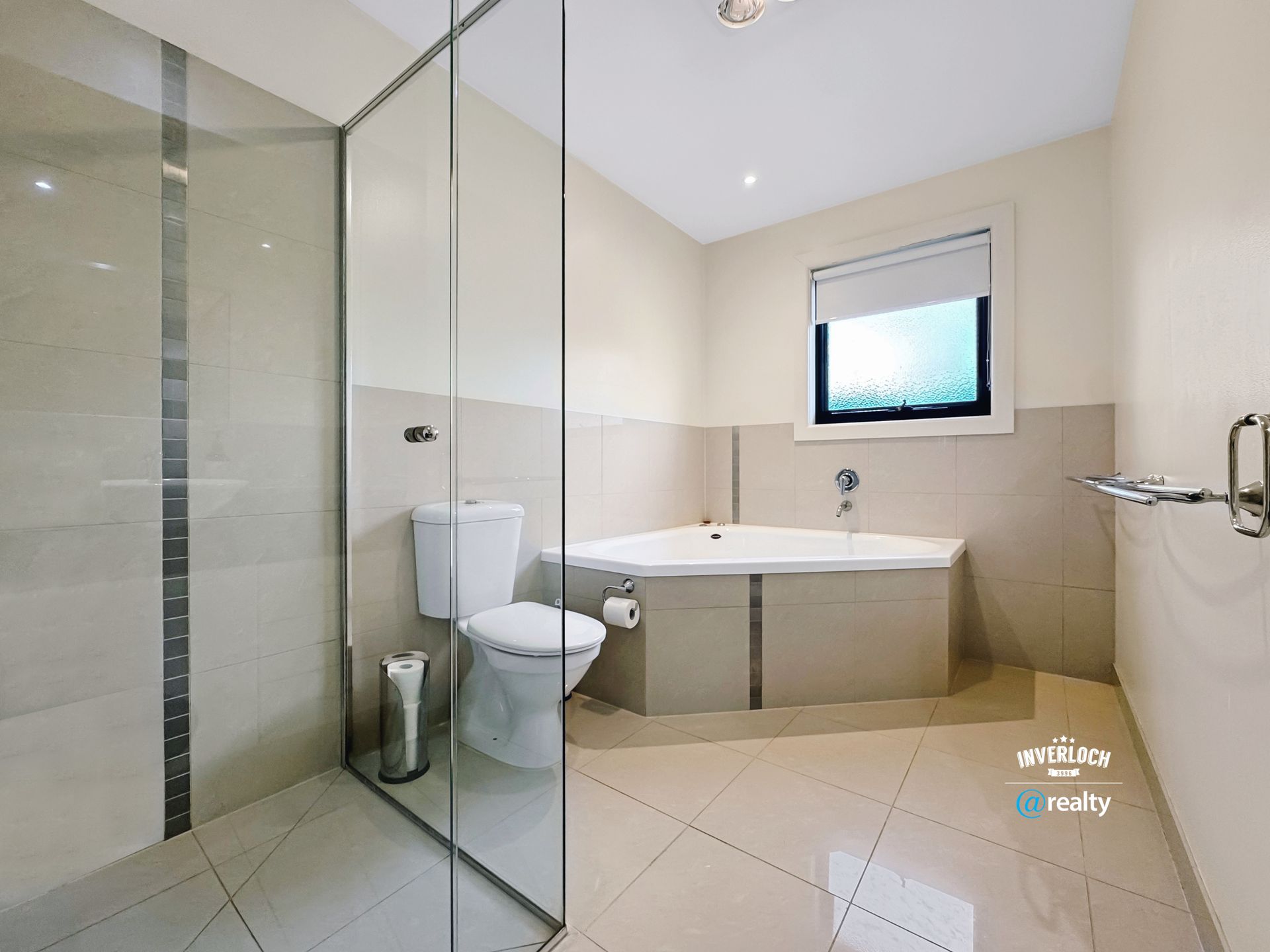 Bathroom with a glass shower, toilet, and a corner bathtub. Light-colored walls and flooring.